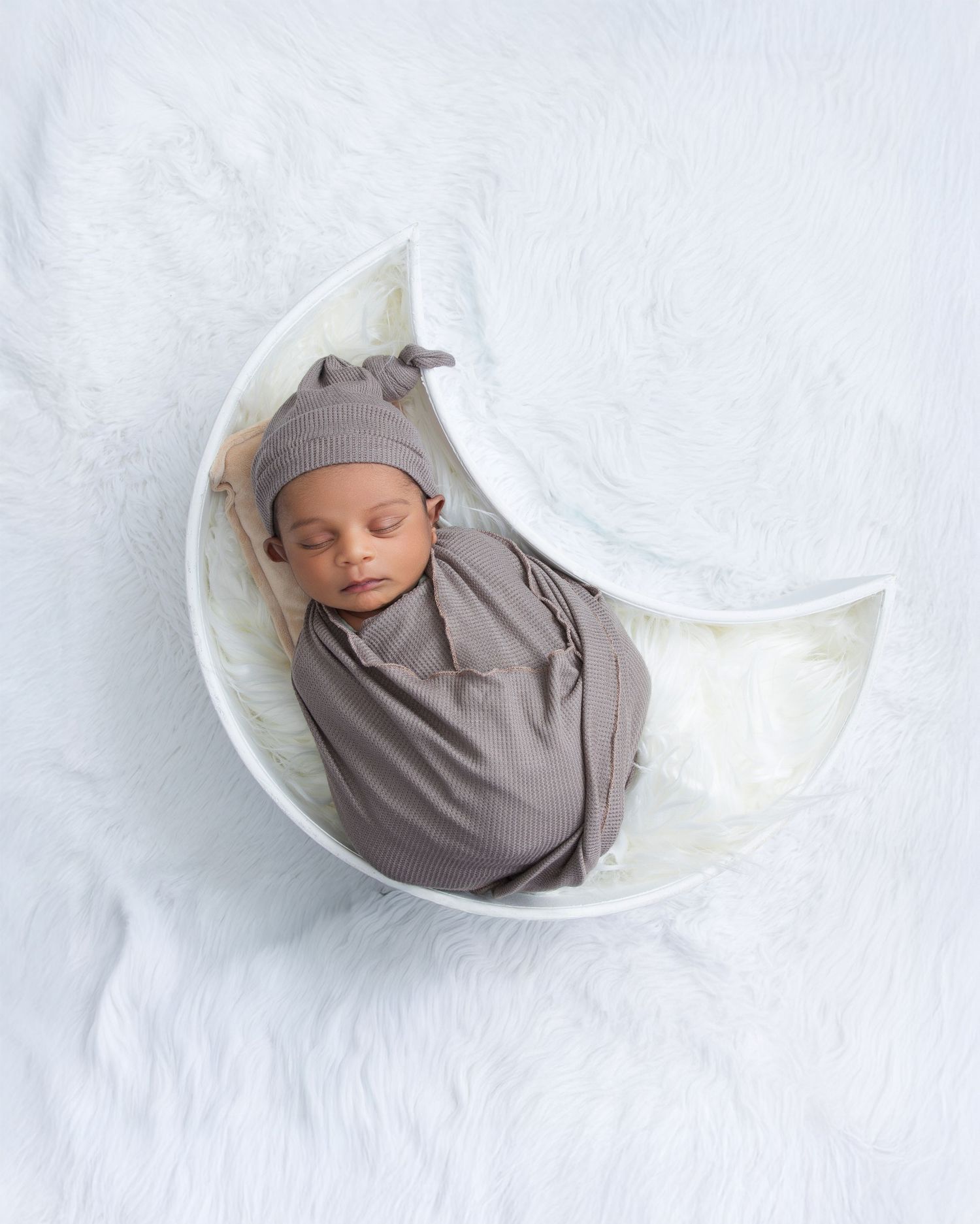 Peaceful sleeping newborn swaddled in gray wrap nestled in white blanket on light backdrop.