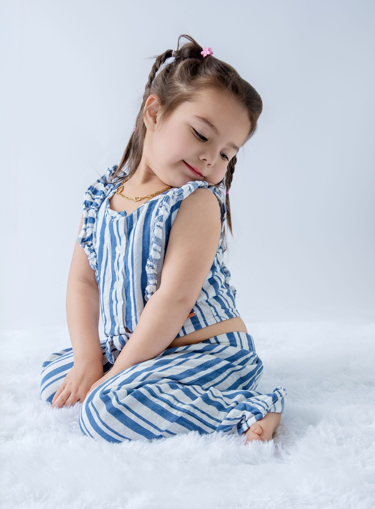 Young child in blue striped dress posing playfully on white floor.