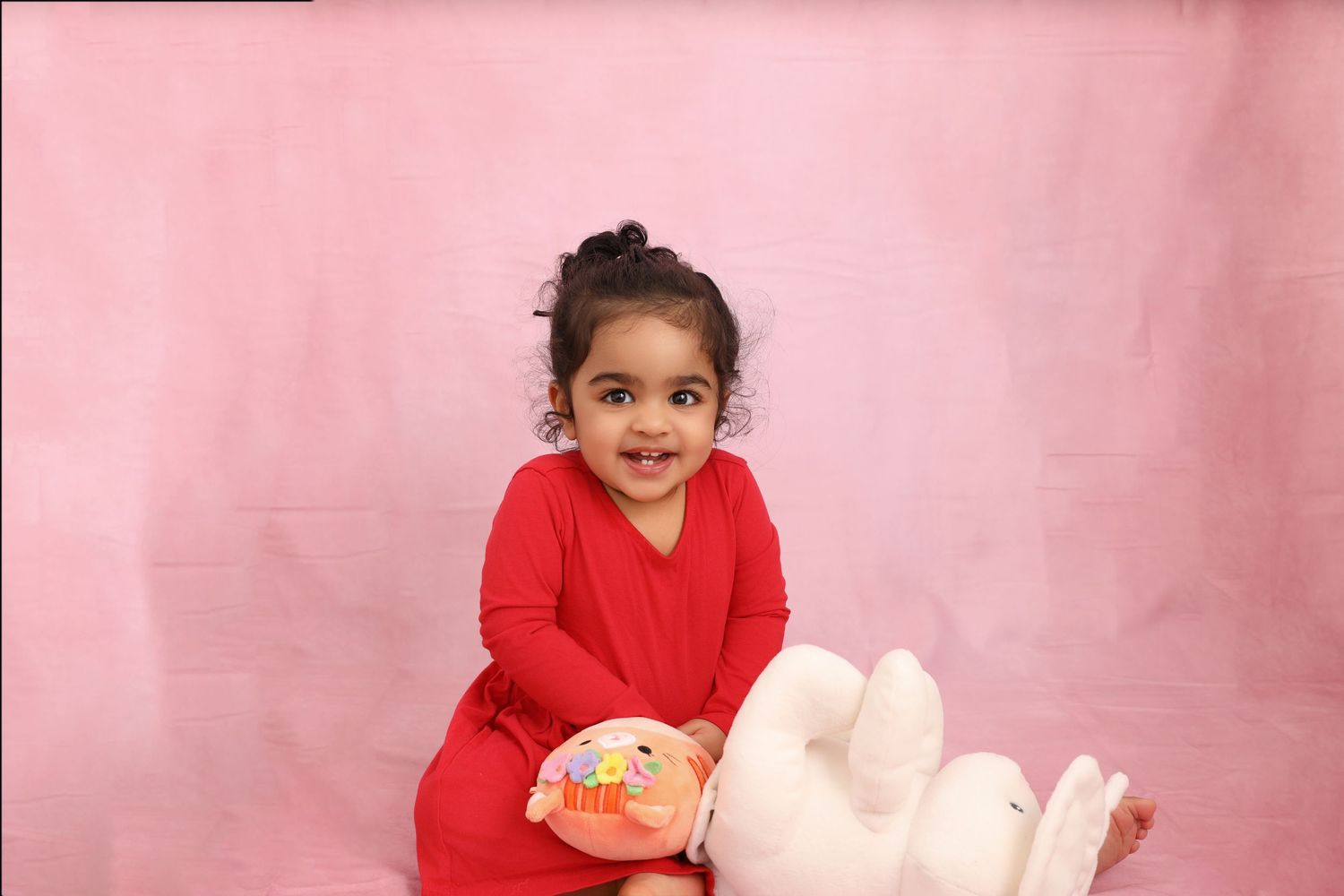 Child wearing red outfit holding toy during studio photo session with pink backdrop.