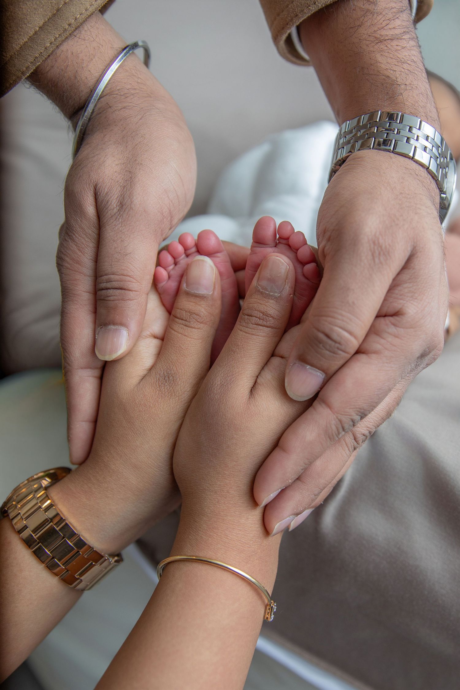 Close up view of two hands holding and examining tiny newborn baby fingers against a white background.