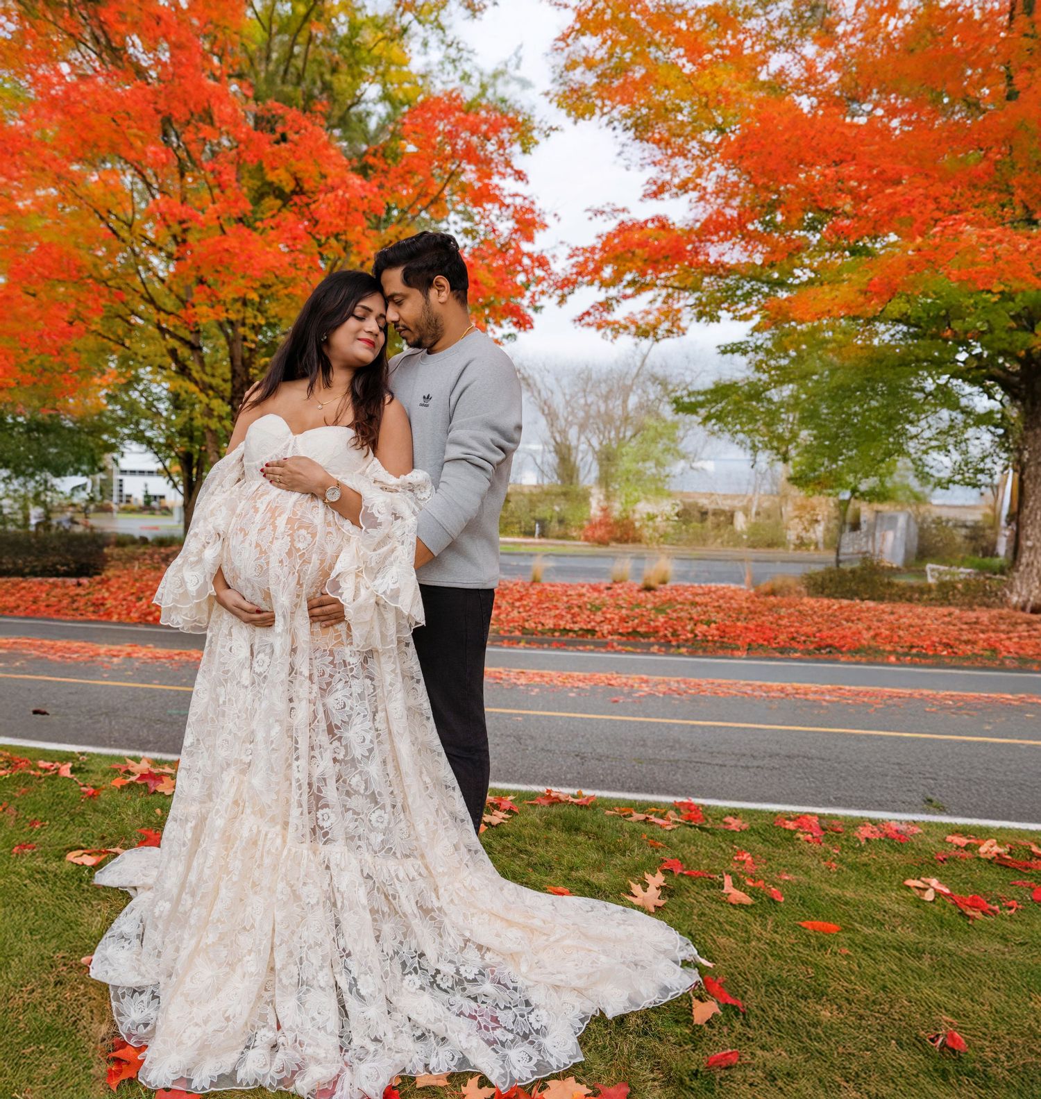 A couple embraces among vibrant red autumn maple trees along a scenic road during fall season.