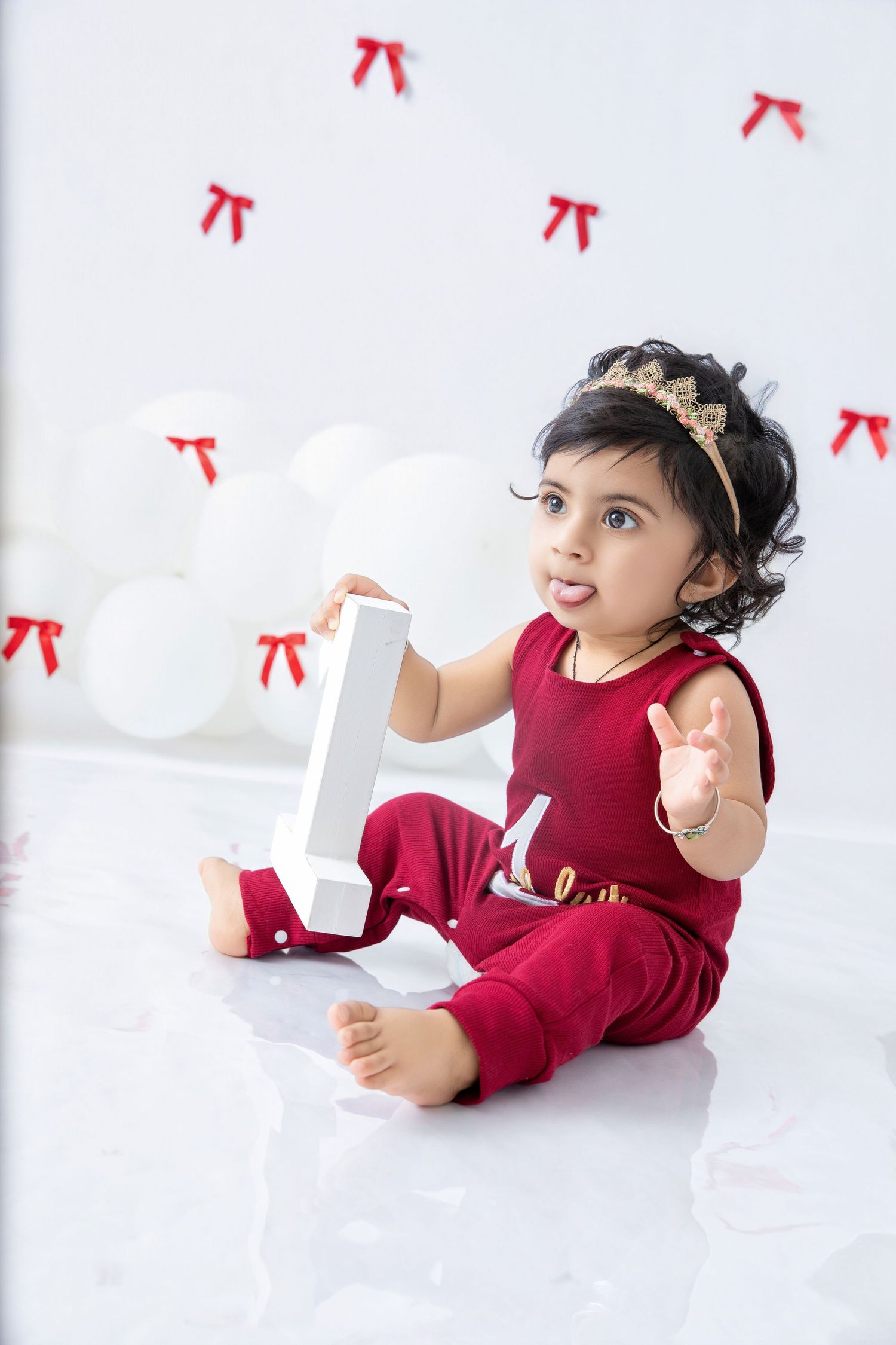 A child in burgundy outfit poses playfully on white floor during photo session.