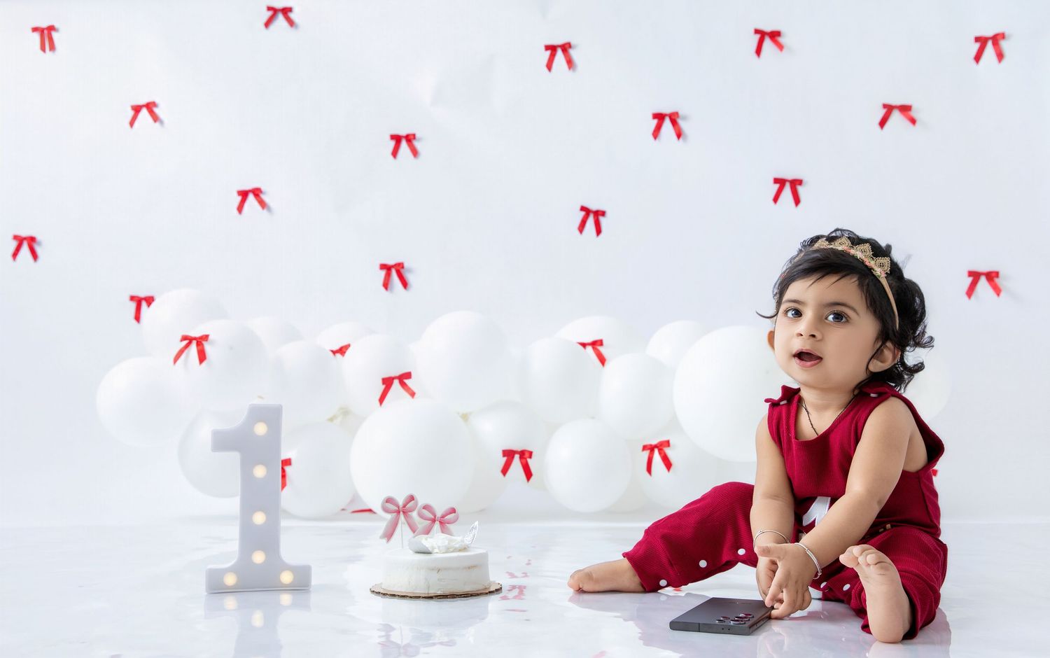 Baby in burgundy outfit reaching towards cake during photo session.
