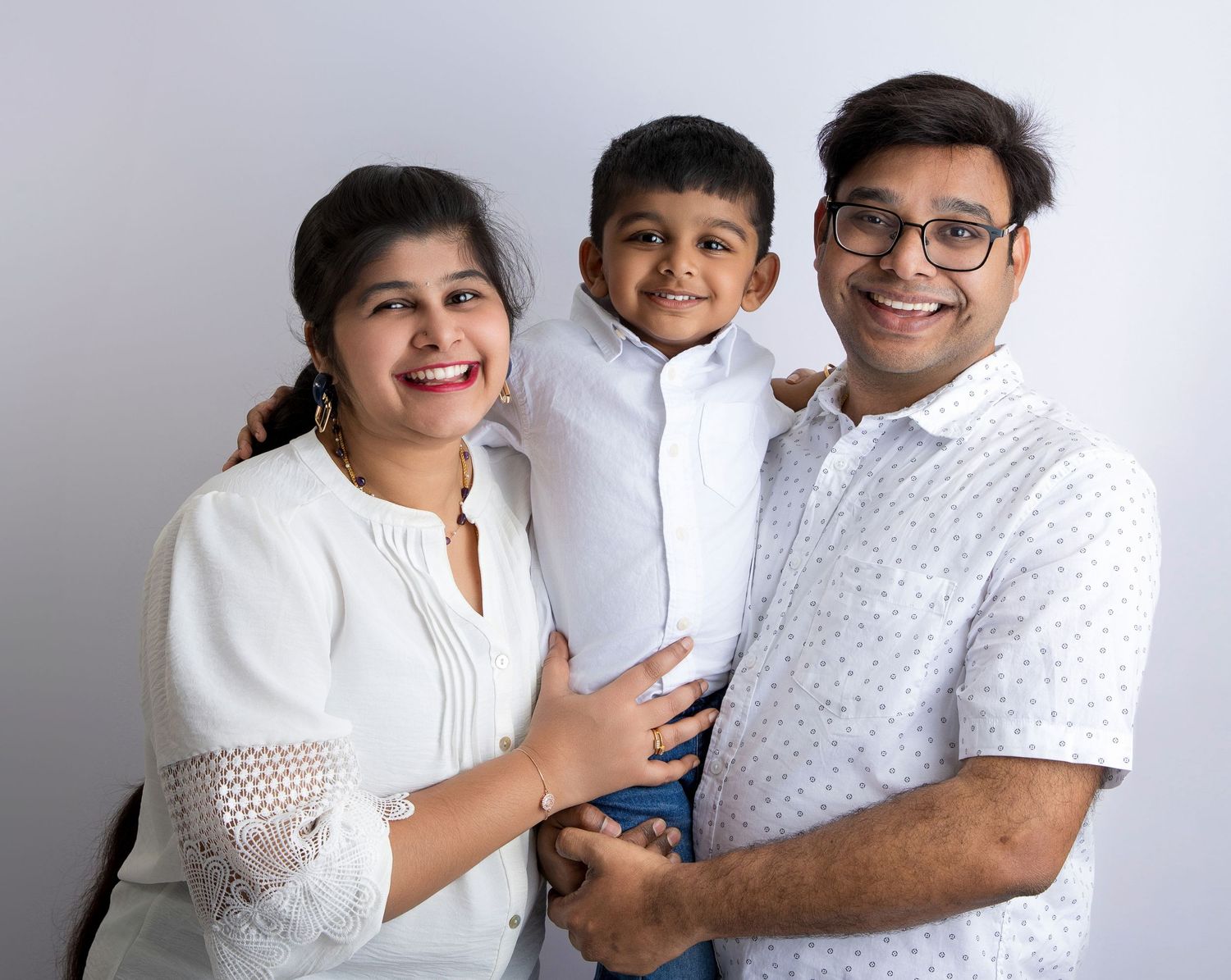 Family wearing white outfits posing together against a light background for a portrait session.