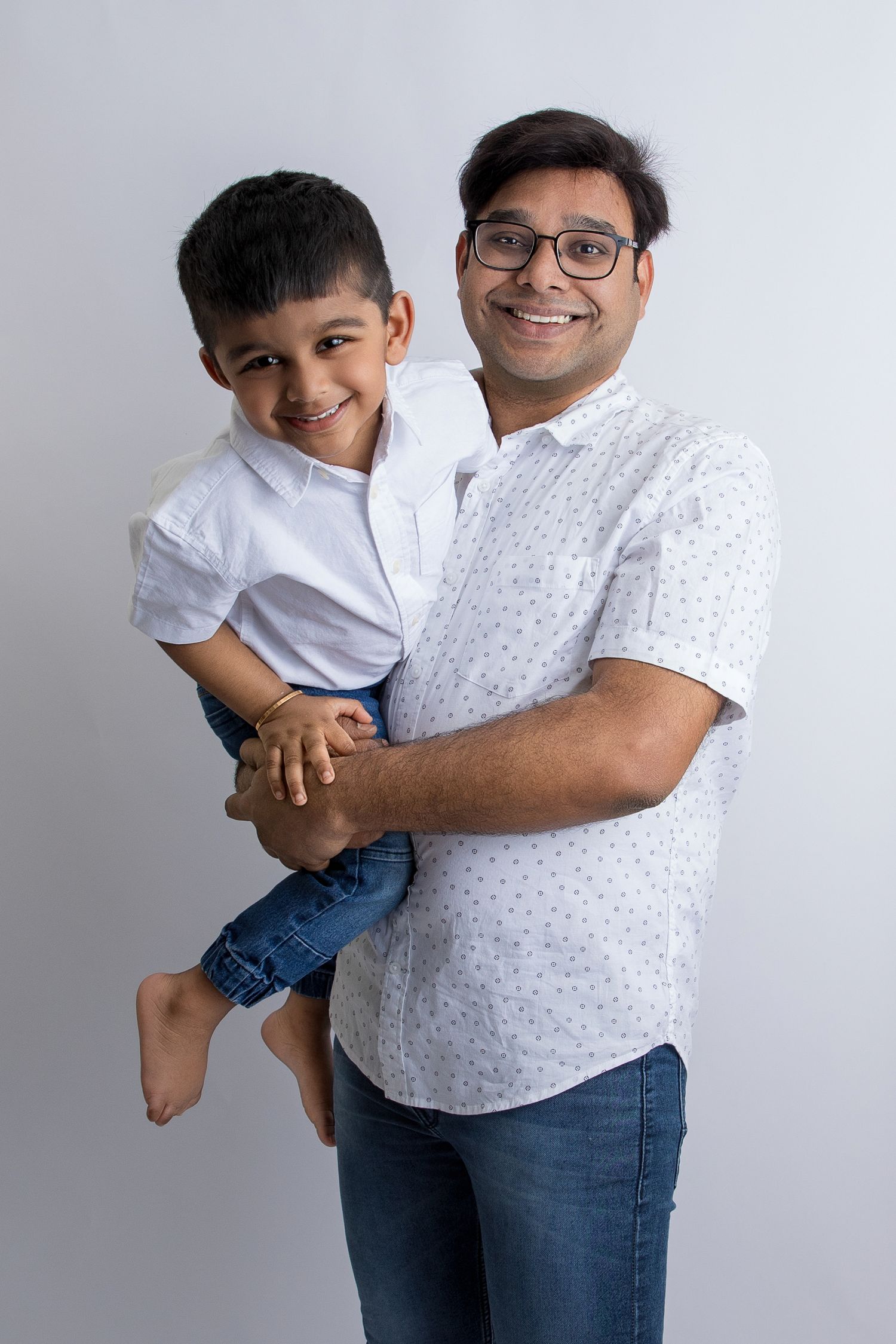Father and son in white shirts share playful moments against white backdrop.