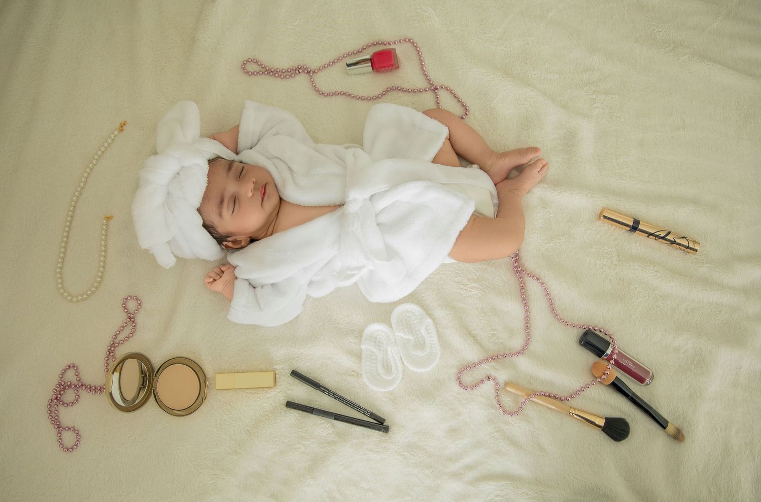 Flatlay composition of baby items including clothing and accessories on white fabric.