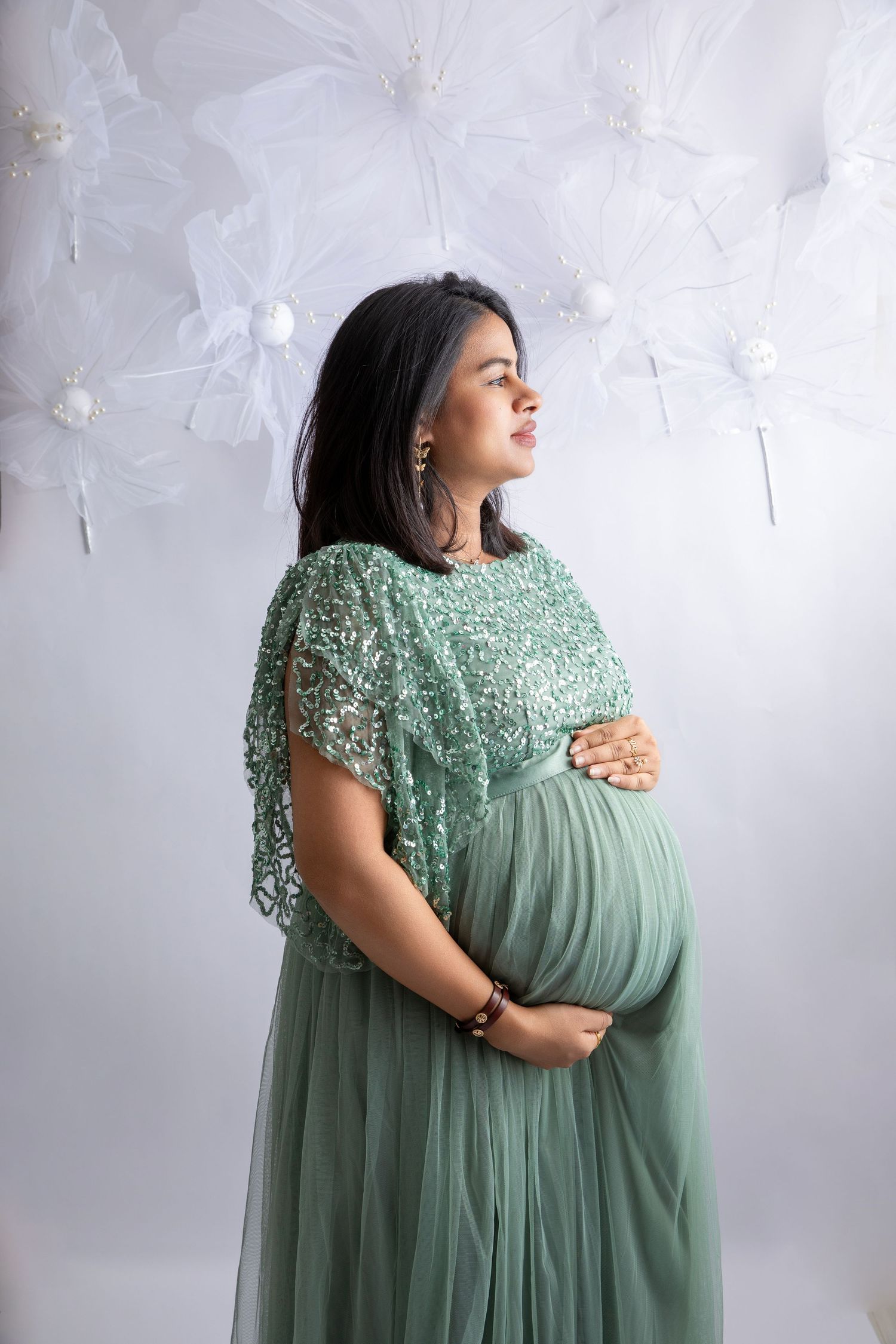 Ethereal maternity portraits in sage green lace gown against textured white backdrop.
