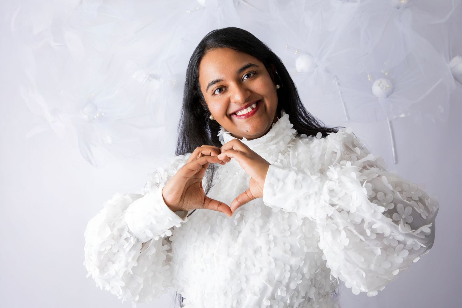 A cozy white textured sweater styled against a light background with heart hand gesture.