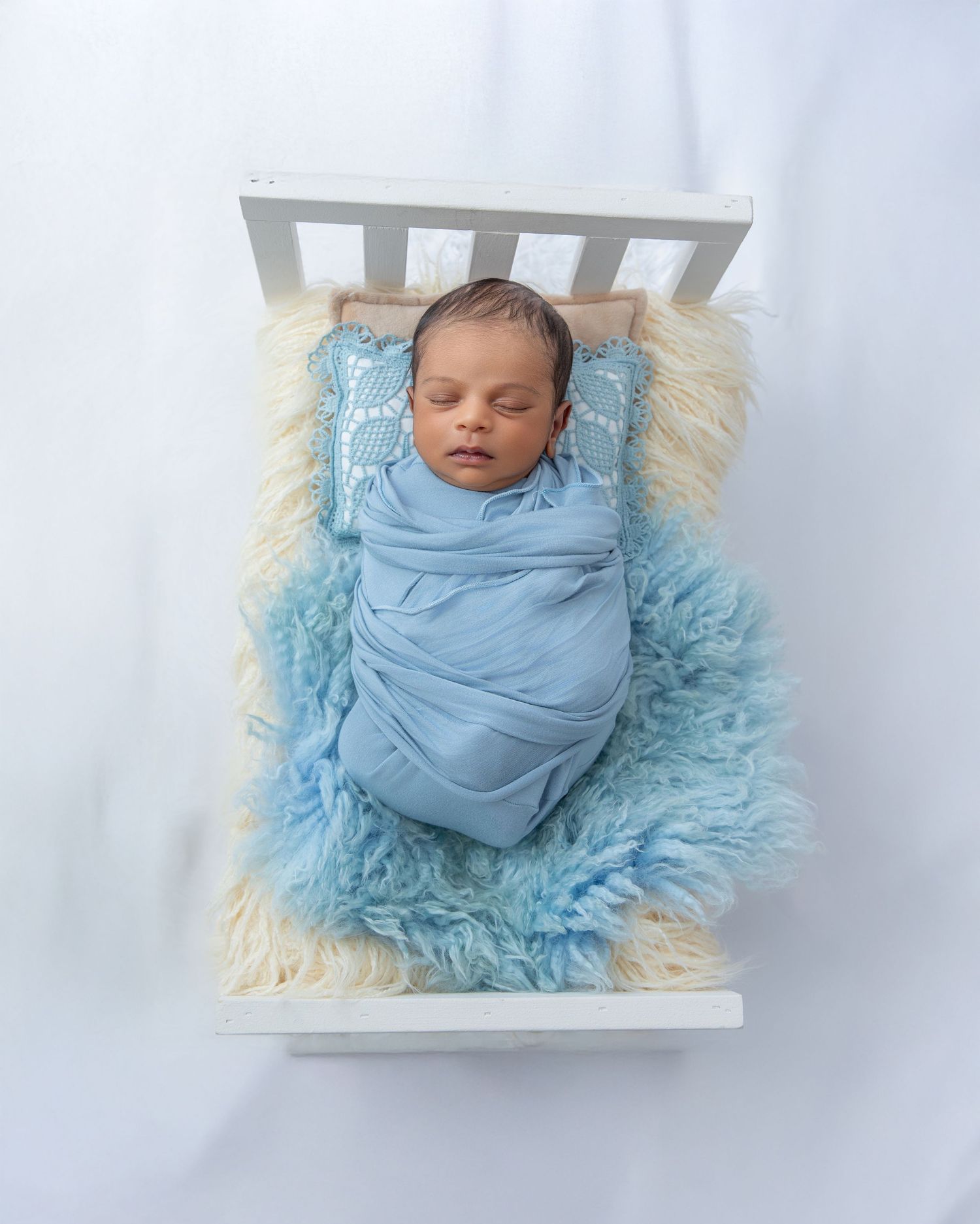 Newborn photography series showing baby wrapped in soft blue fabric against fluffy fur backdrop.
