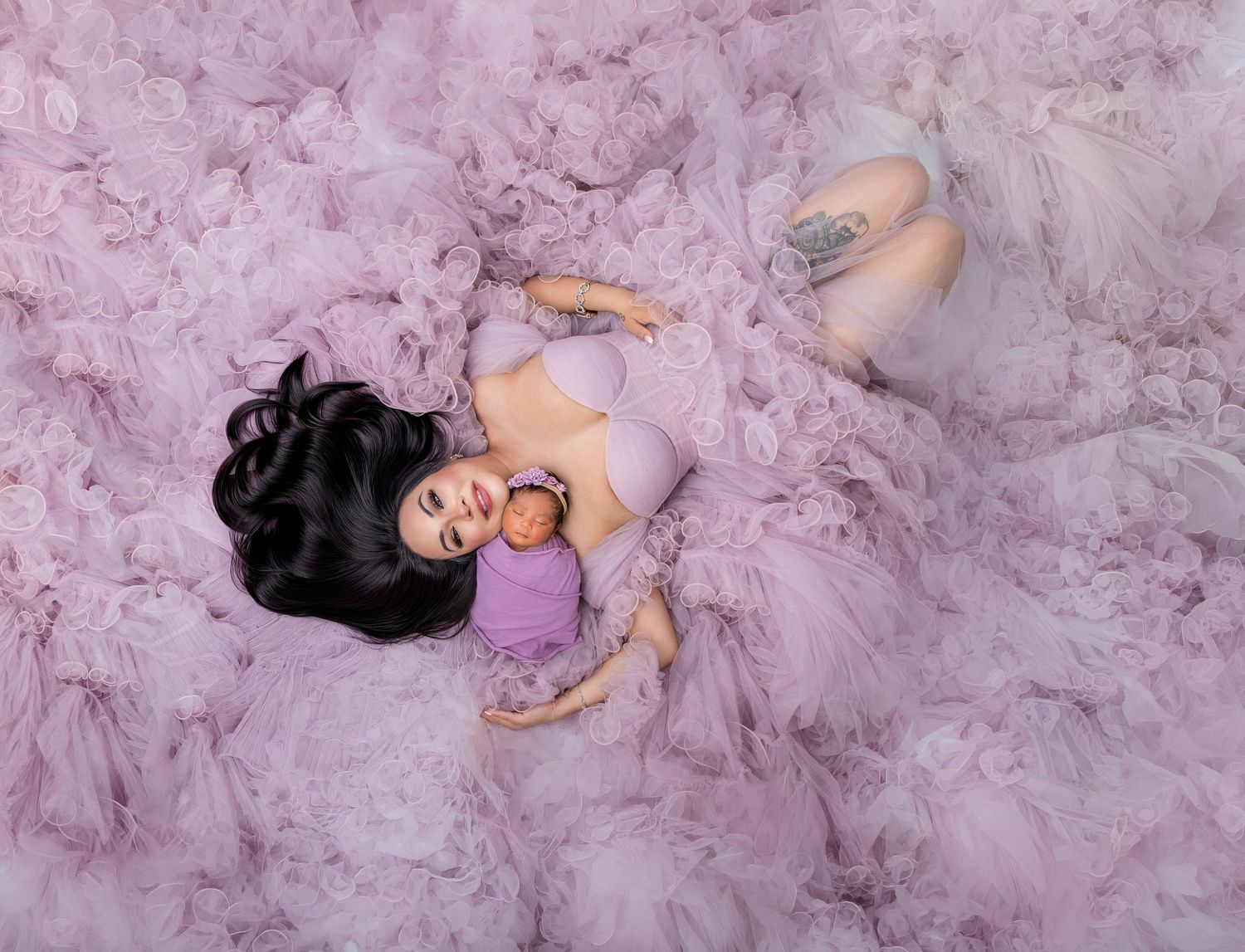 Mother in lavender outfit lying in pink tulle ruffles holding her newborn baby during maternity photo session.