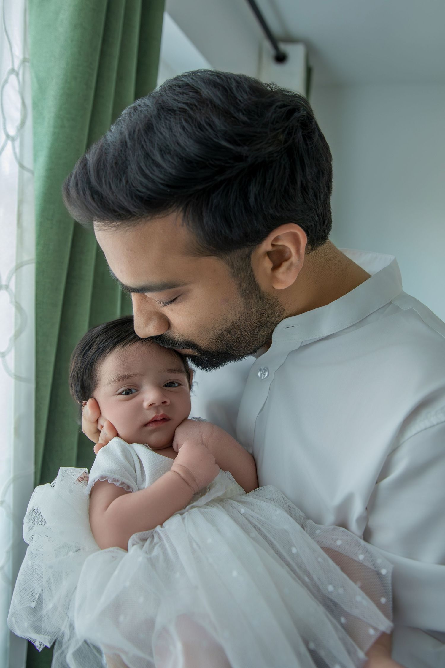 A tender moment in white as a baby in a delicate dress rests against someone wearing light colored clothing.