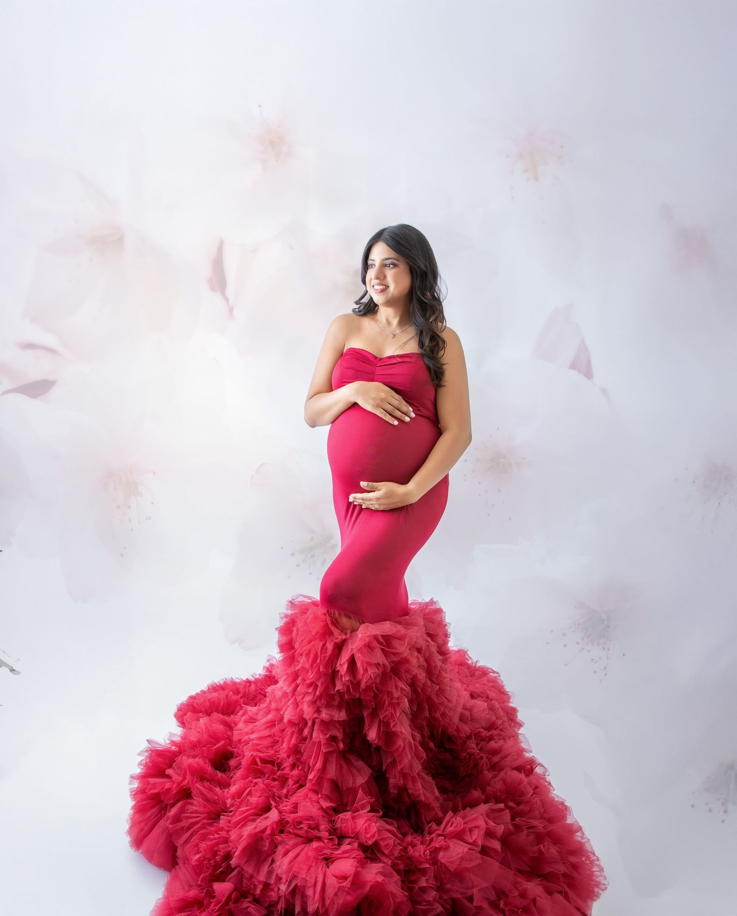 Elegant maternity photo featuring a dramatic red mermaid gown with ruffled tulle skirt against a light ethereal backdrop.