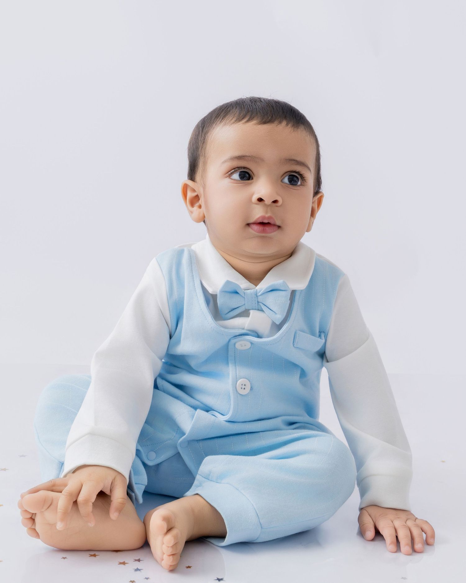 Baby in light blue formal wear crawling on white studio backdrop.