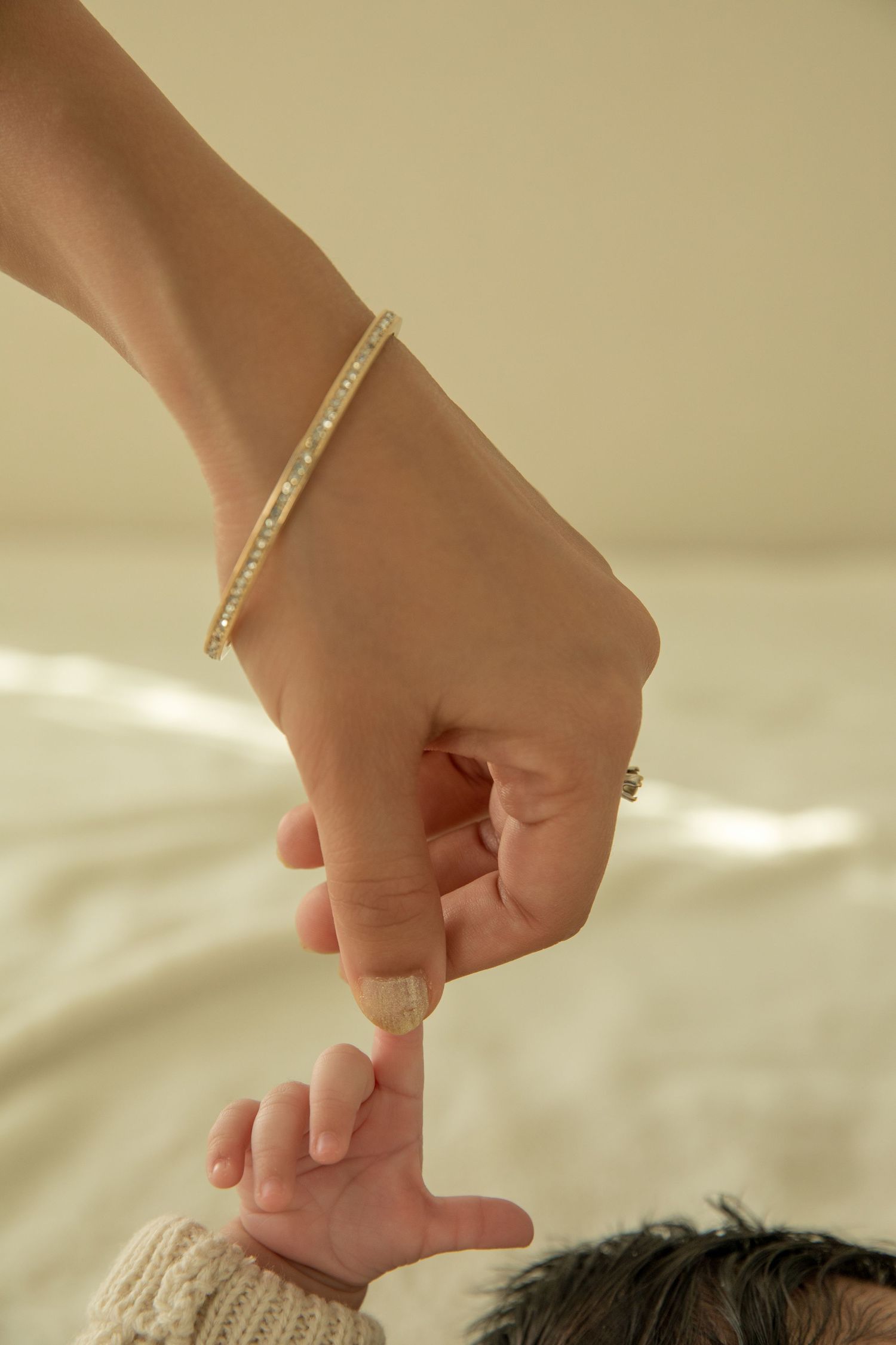 Close-up of hand gently touching baby's tiny fingers against light background.