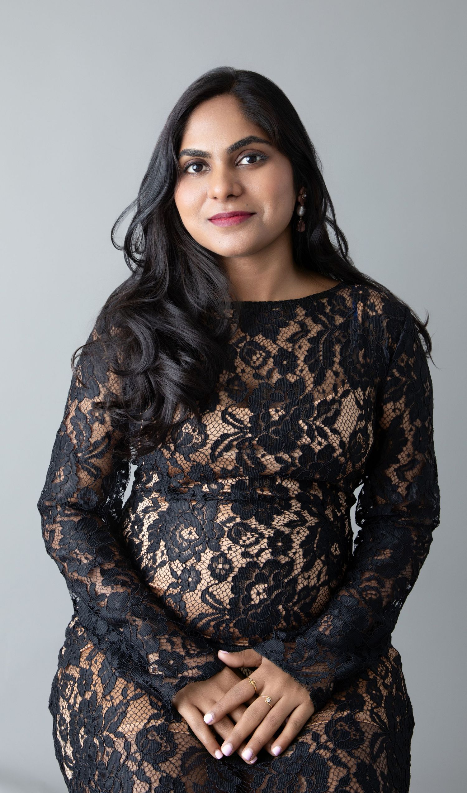 Professional portrait of woman in black lace dress against gray studio backdrop.