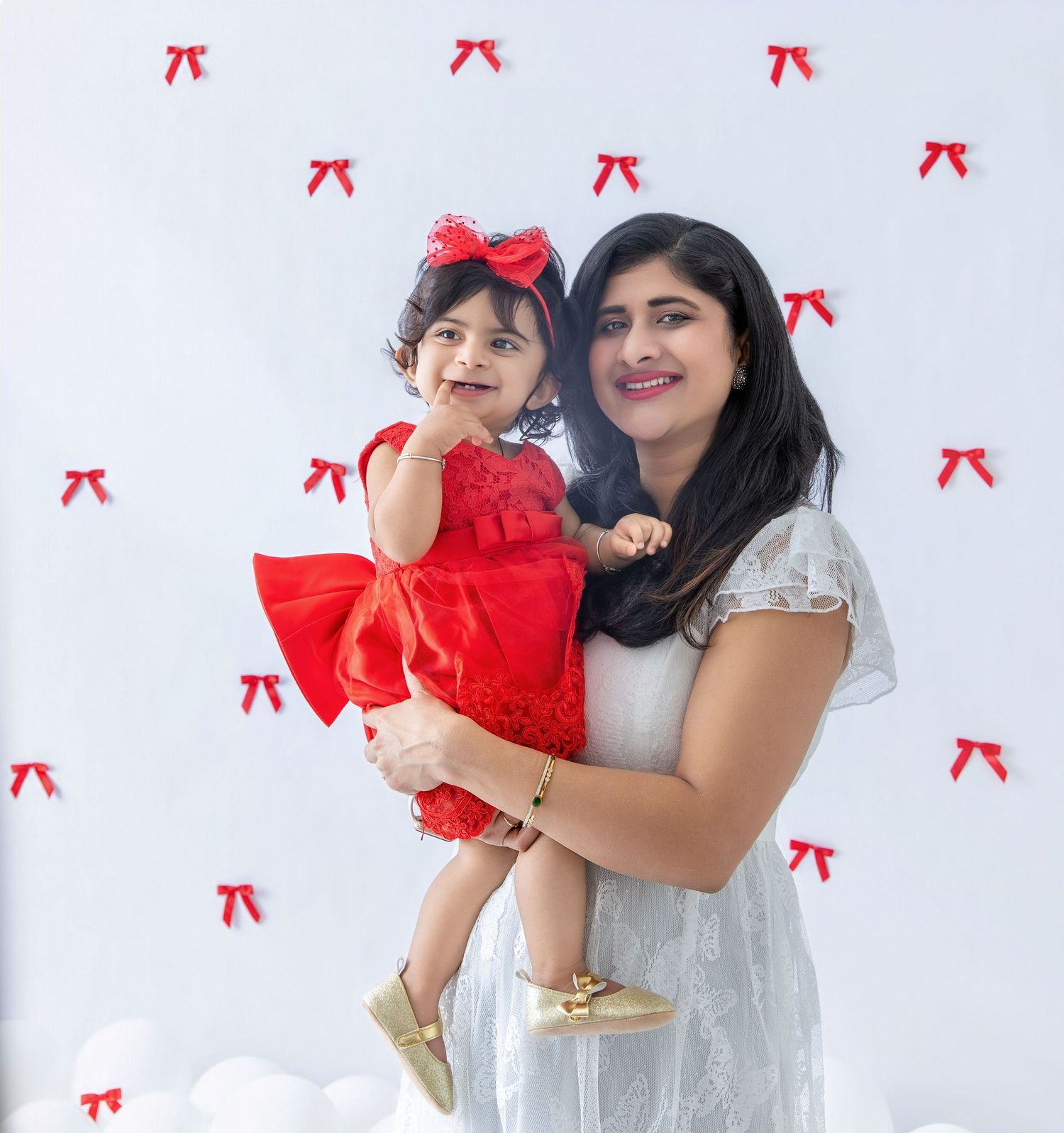 Family members interact playfully against white backdrop with festive red bow pattern.