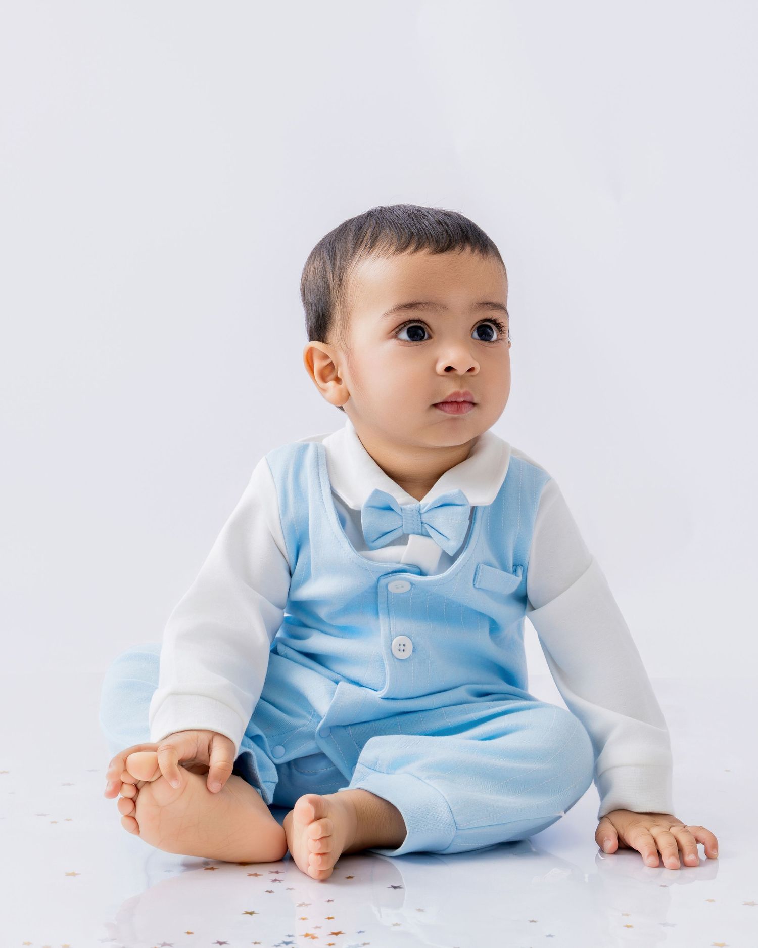 Baby in light blue formal outfit with white sleeves and bow tie sitting against white backdrop.