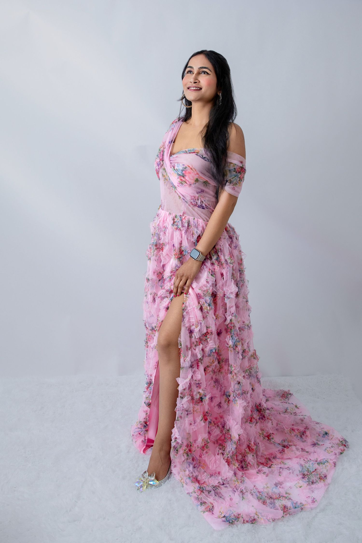 Joyful maternity pose in romantic pink floral gown against studio backdrop.