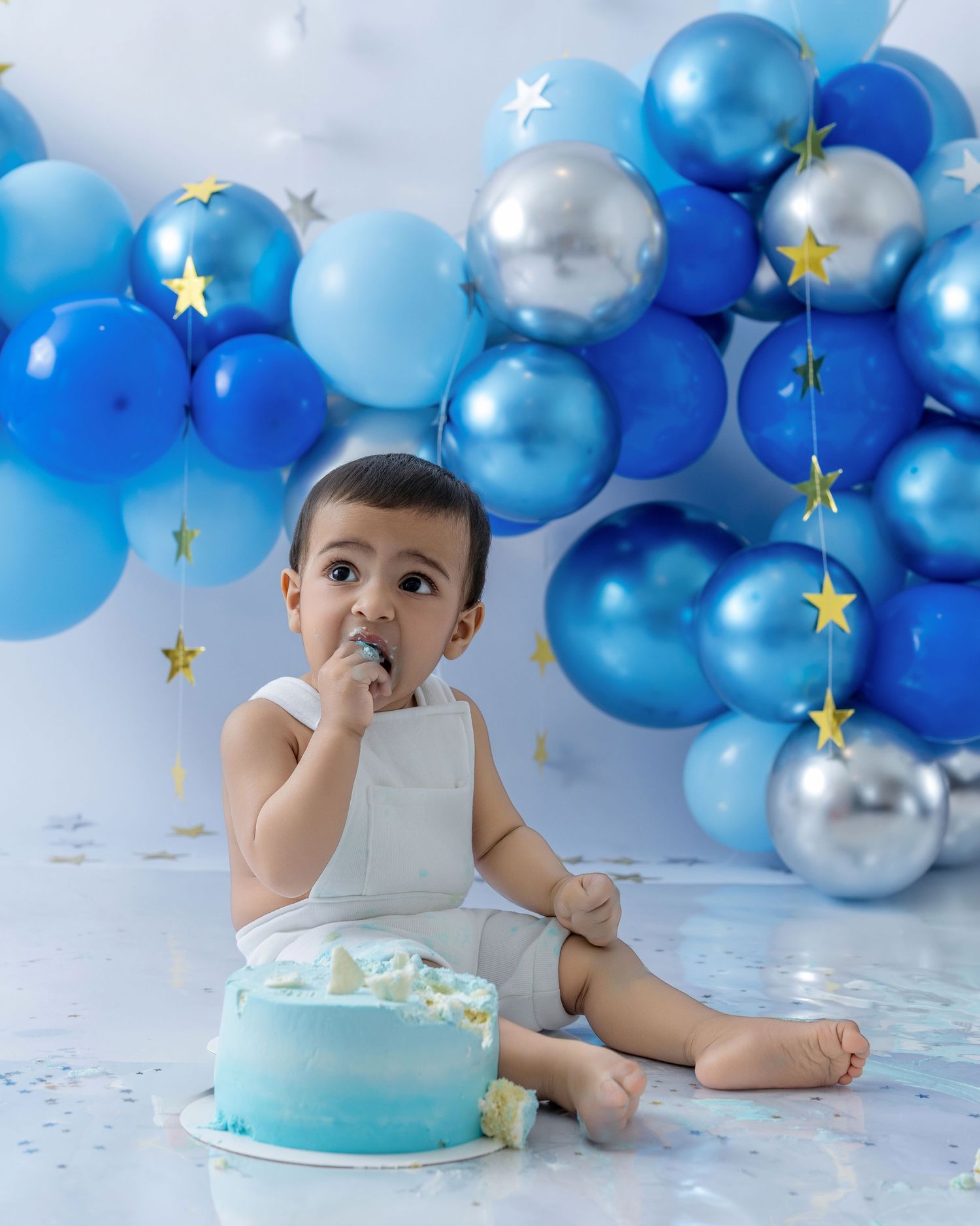 First birthday cake smash photo session with blue and silver balloon arch decorations and a turquoise cake.