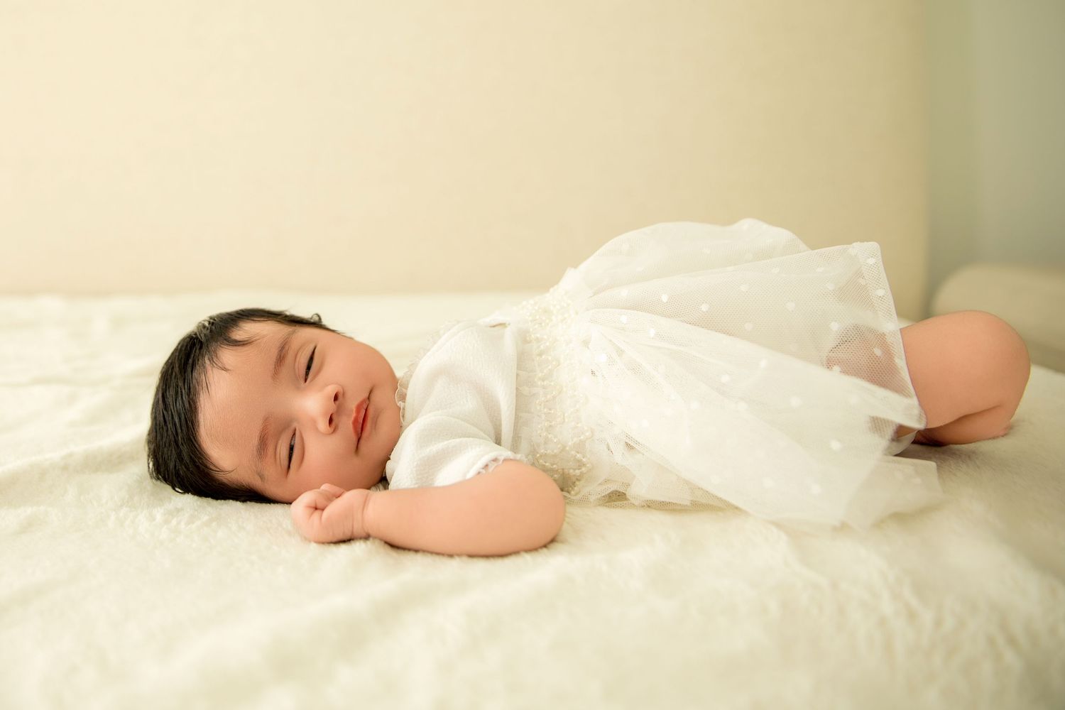 A baby lies peacefully sleeping on white bedding in a series of connected photos showing different angles.