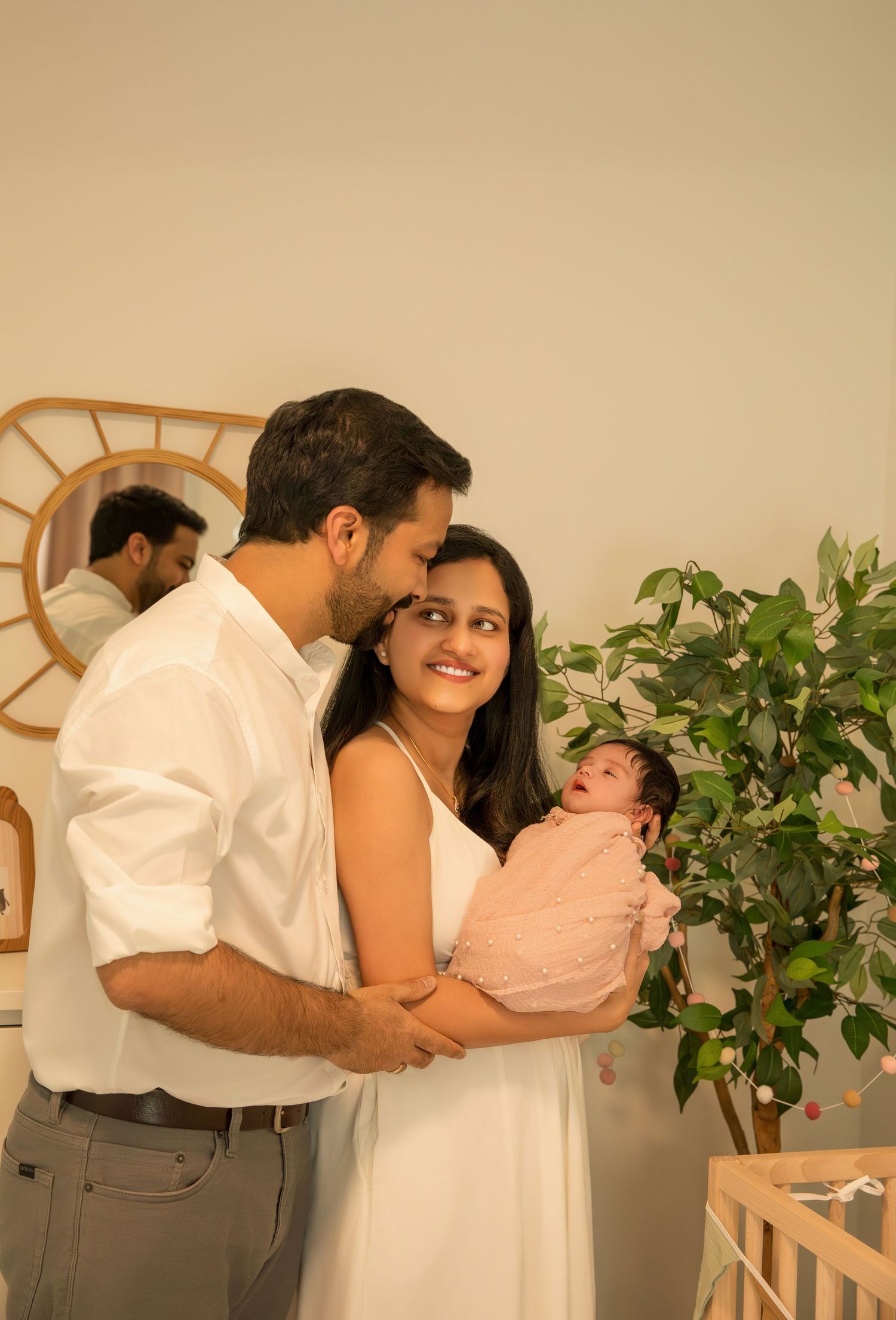 A family poses together in a minimalist studio setting with indoor plants and white decor.