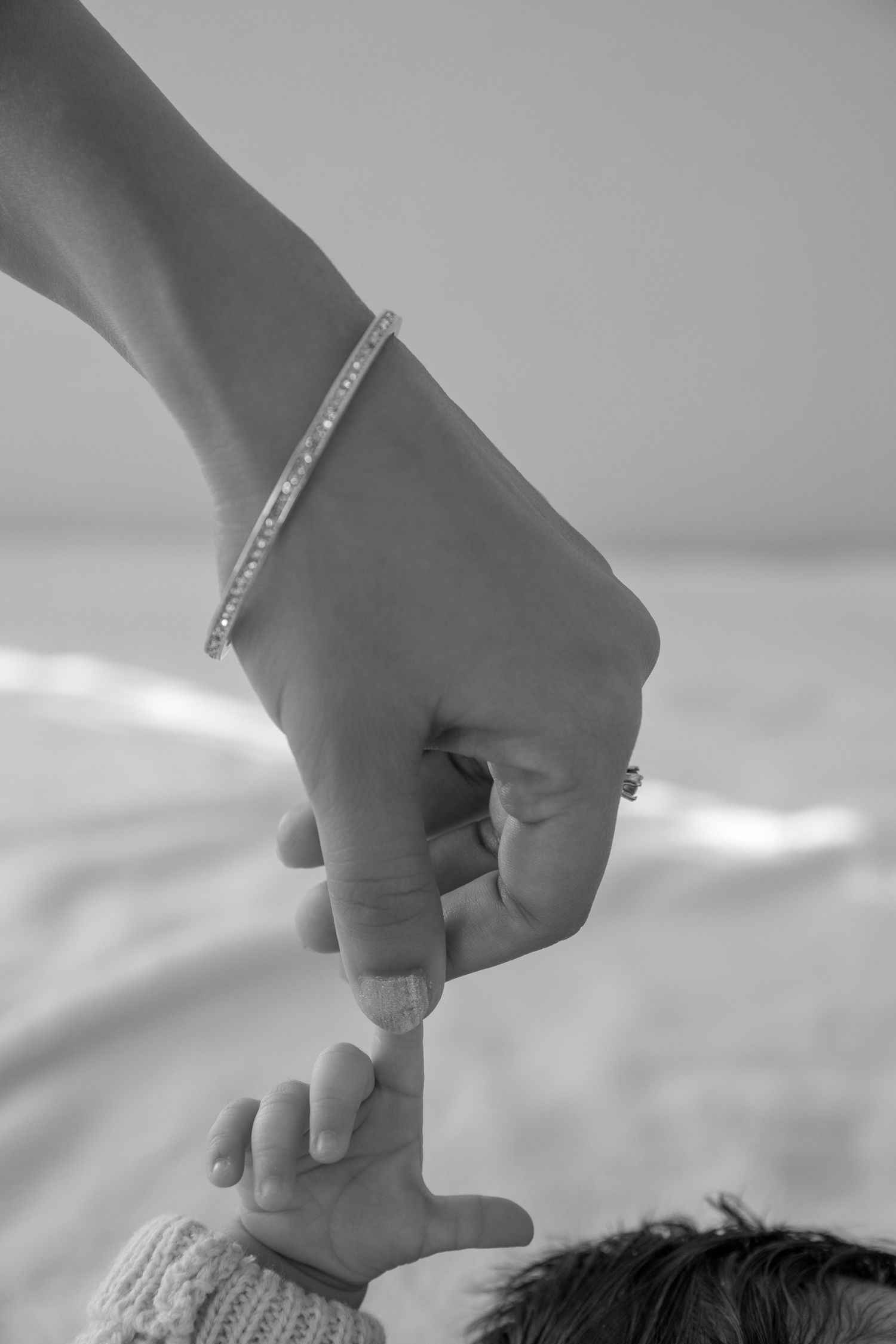 A delicate hand wearing a bracelet touches a small baby foot in a knitted garment.