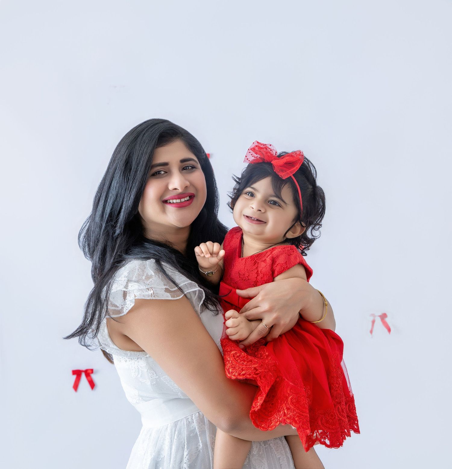 Family embracing in coordinated white and red outfits against light background.