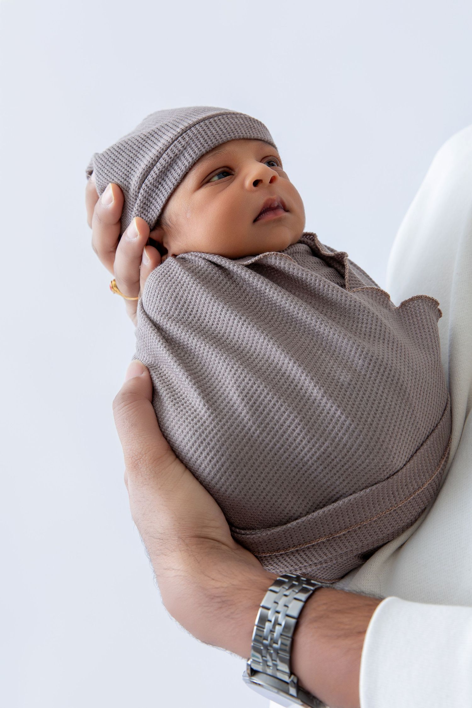 Close-up shots of hands gently cradling a newborn baby wrapped in soft grey knit fabric.