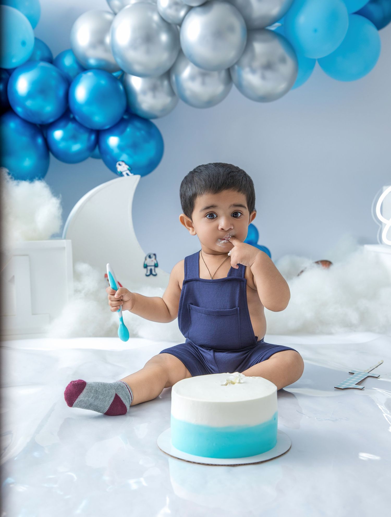 A first birthday celebration setup with blue balloon garland, crescent moon prop, and turquoise cake.