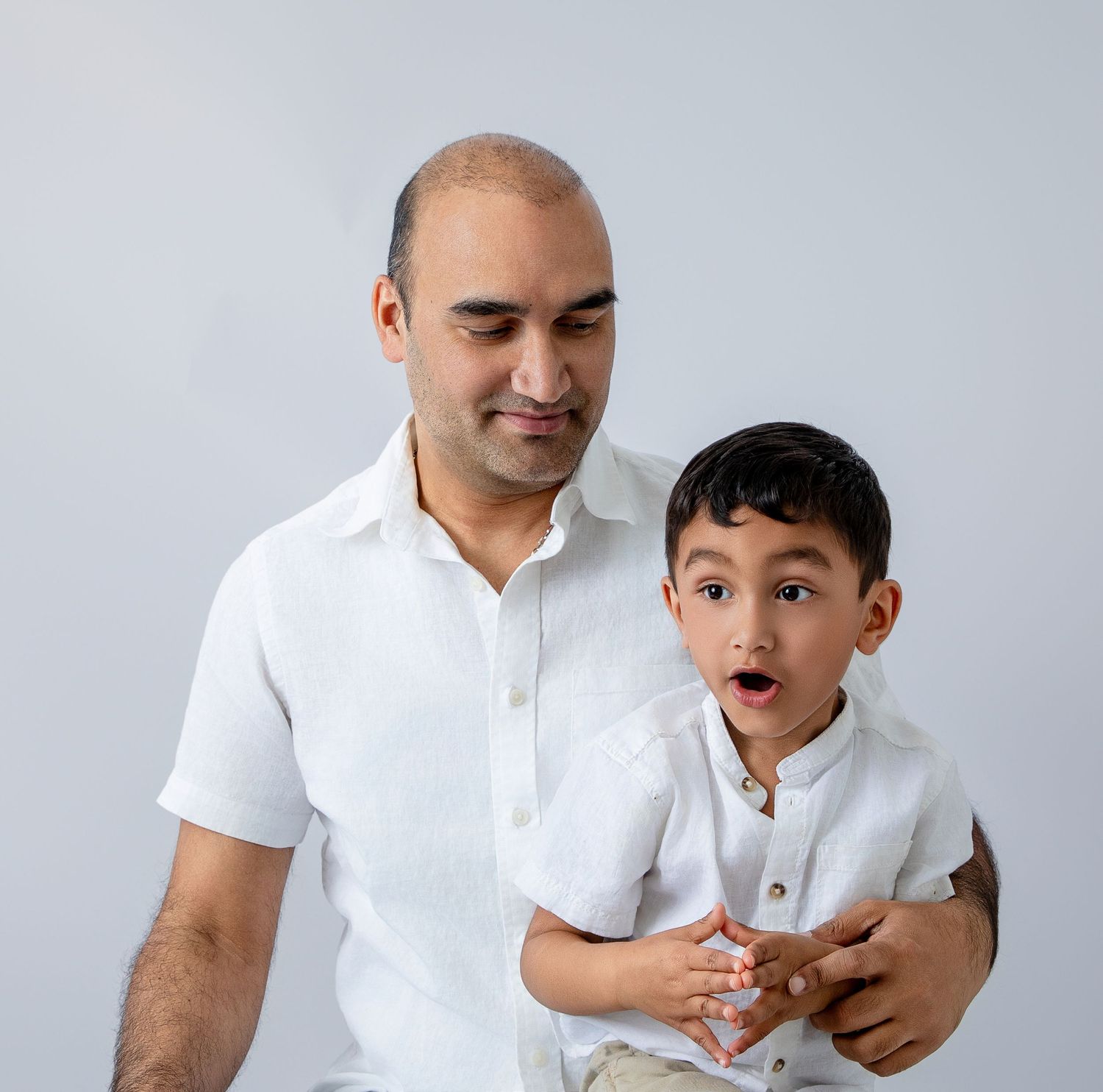 Father and son sharing playful expressions in matching white shirts.