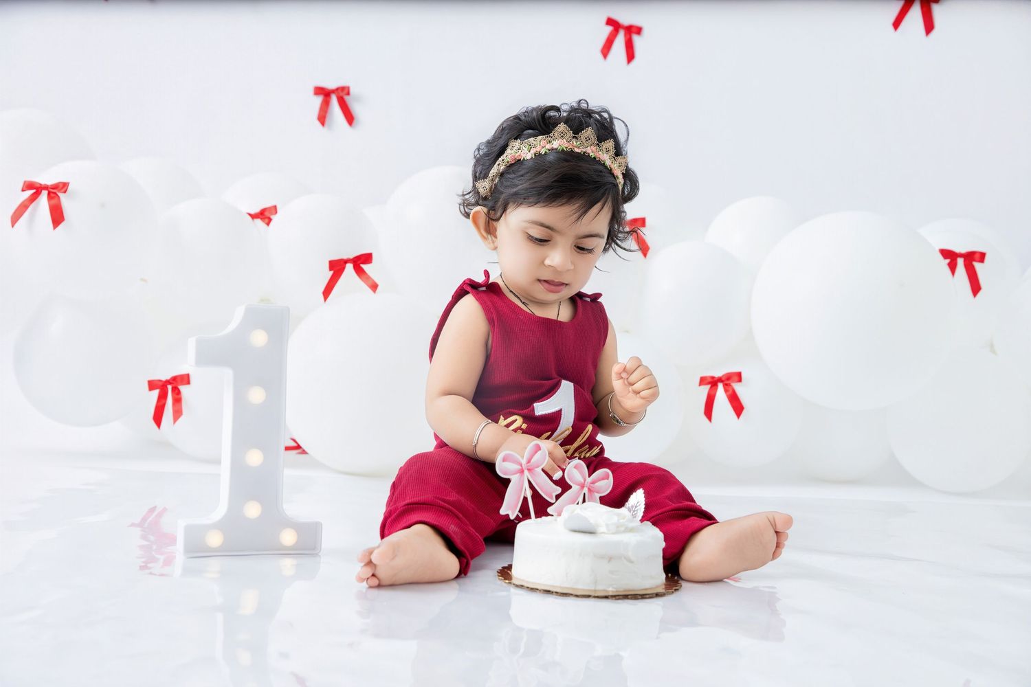 First birthday photo shoot with white cake and red bow decorations.