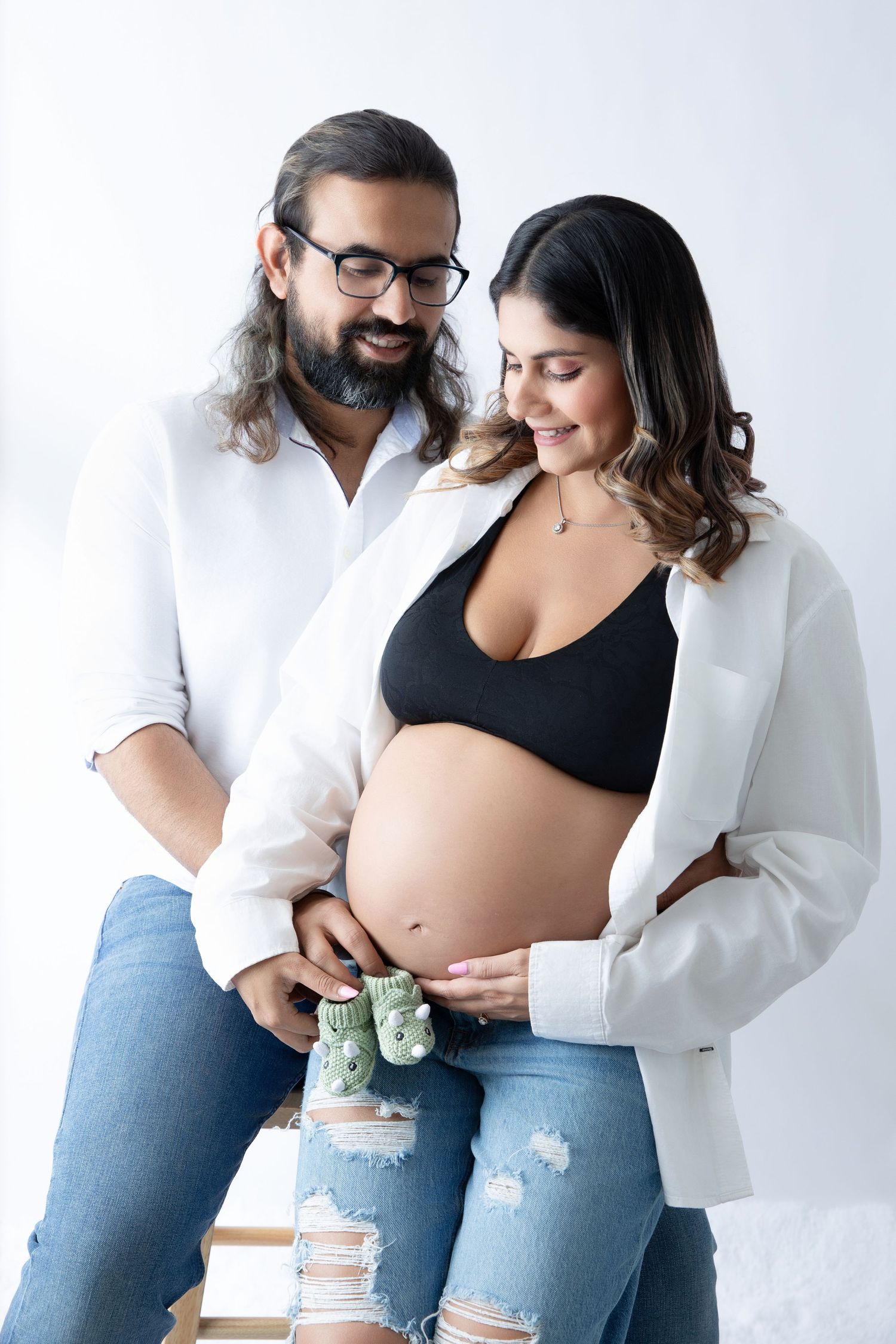 Expecting couple in casual attire sharing tender moments during maternity photoshoot.