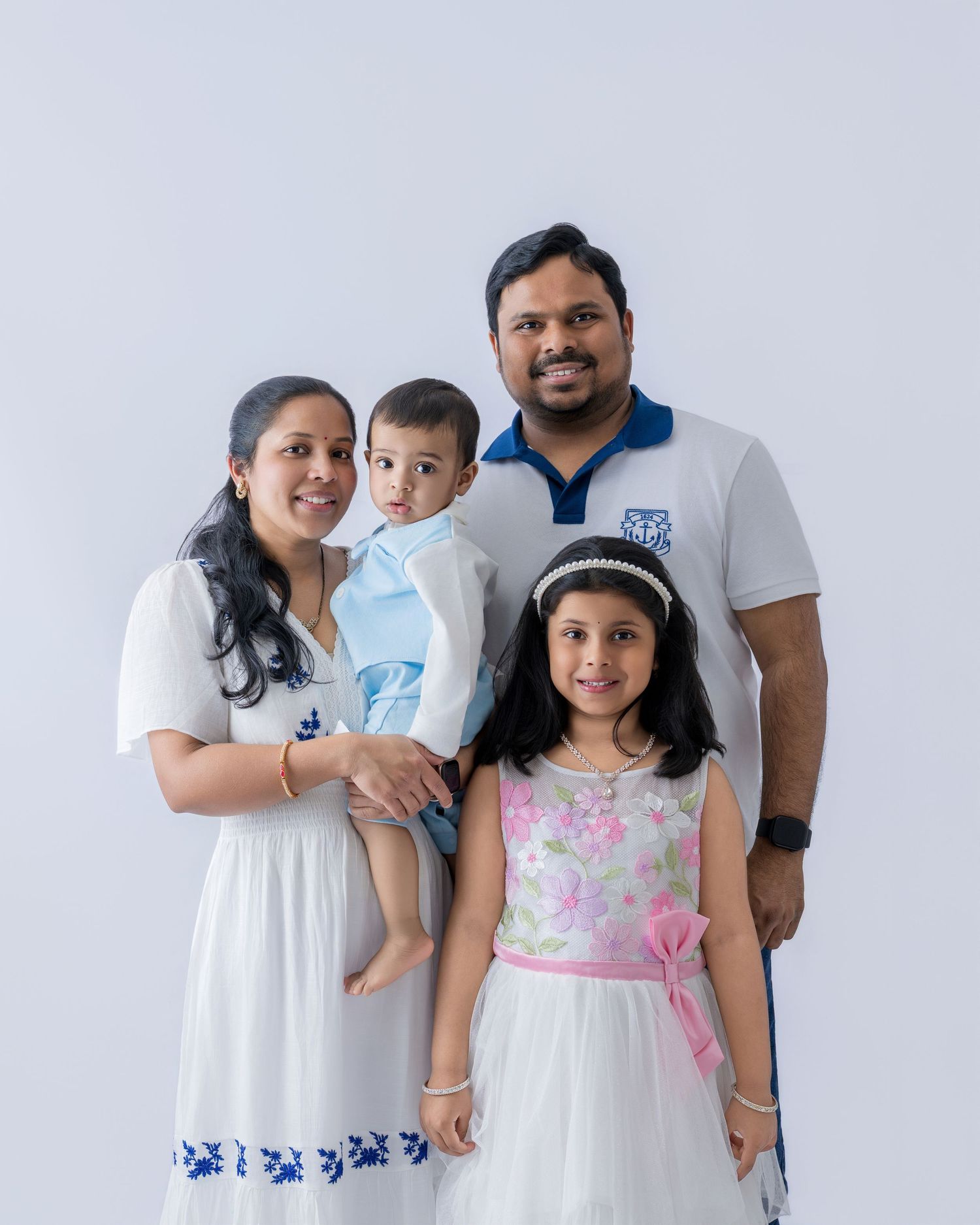 A family in coordinating white outfits poses together against a light gray studio backdrop.