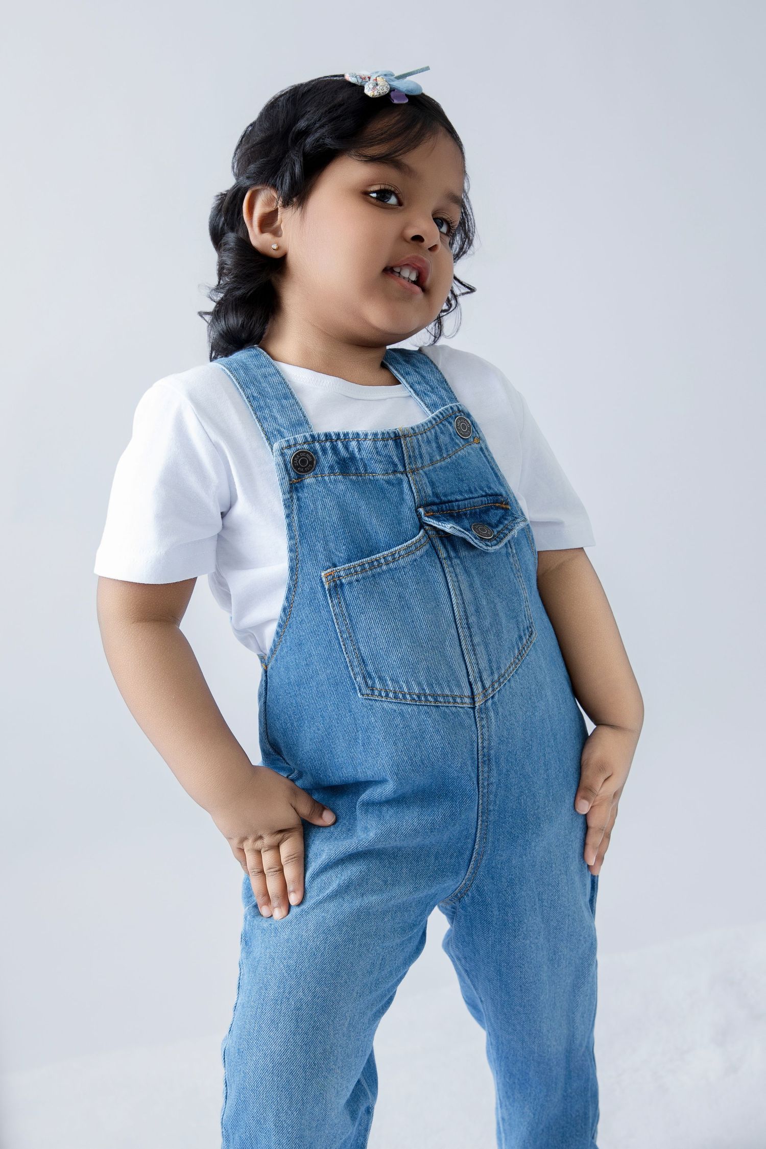 Candid shots of child in denim overalls striking various poses against white backdrop.