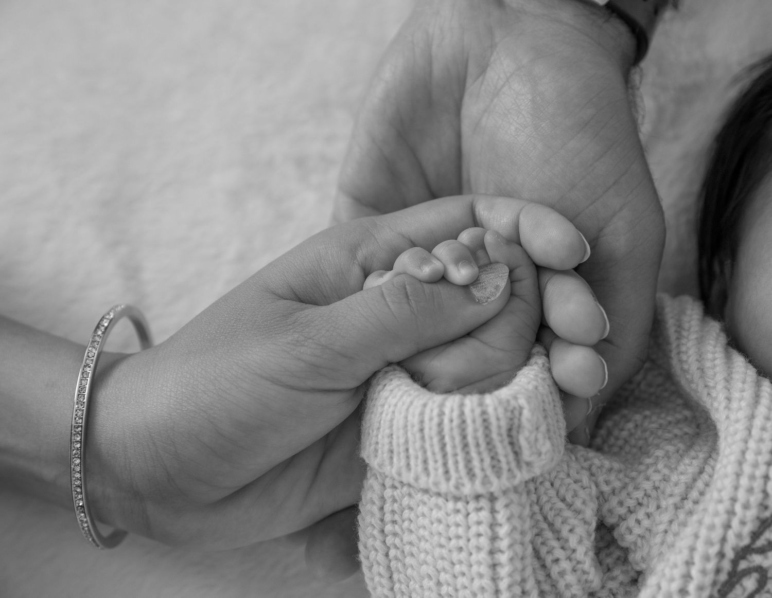A tender black and white image of adult hands gently holding a tiny baby's foot in a knit bootie.