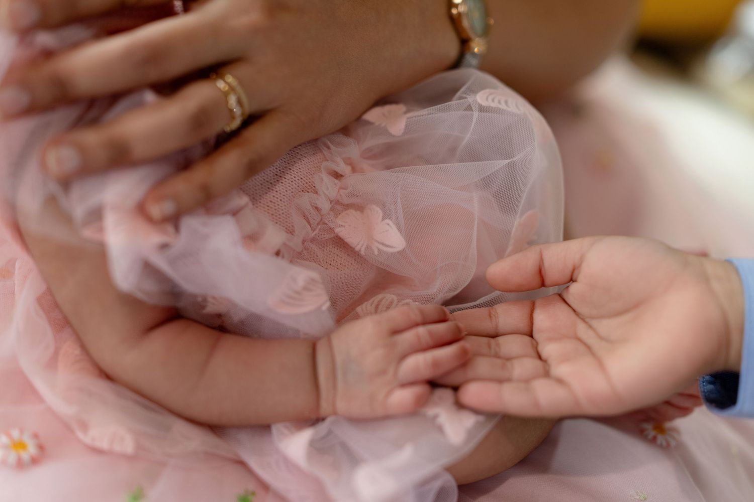 Close-up of newborn baby hands in pink tulle dress being held by sibling during photoshoot.