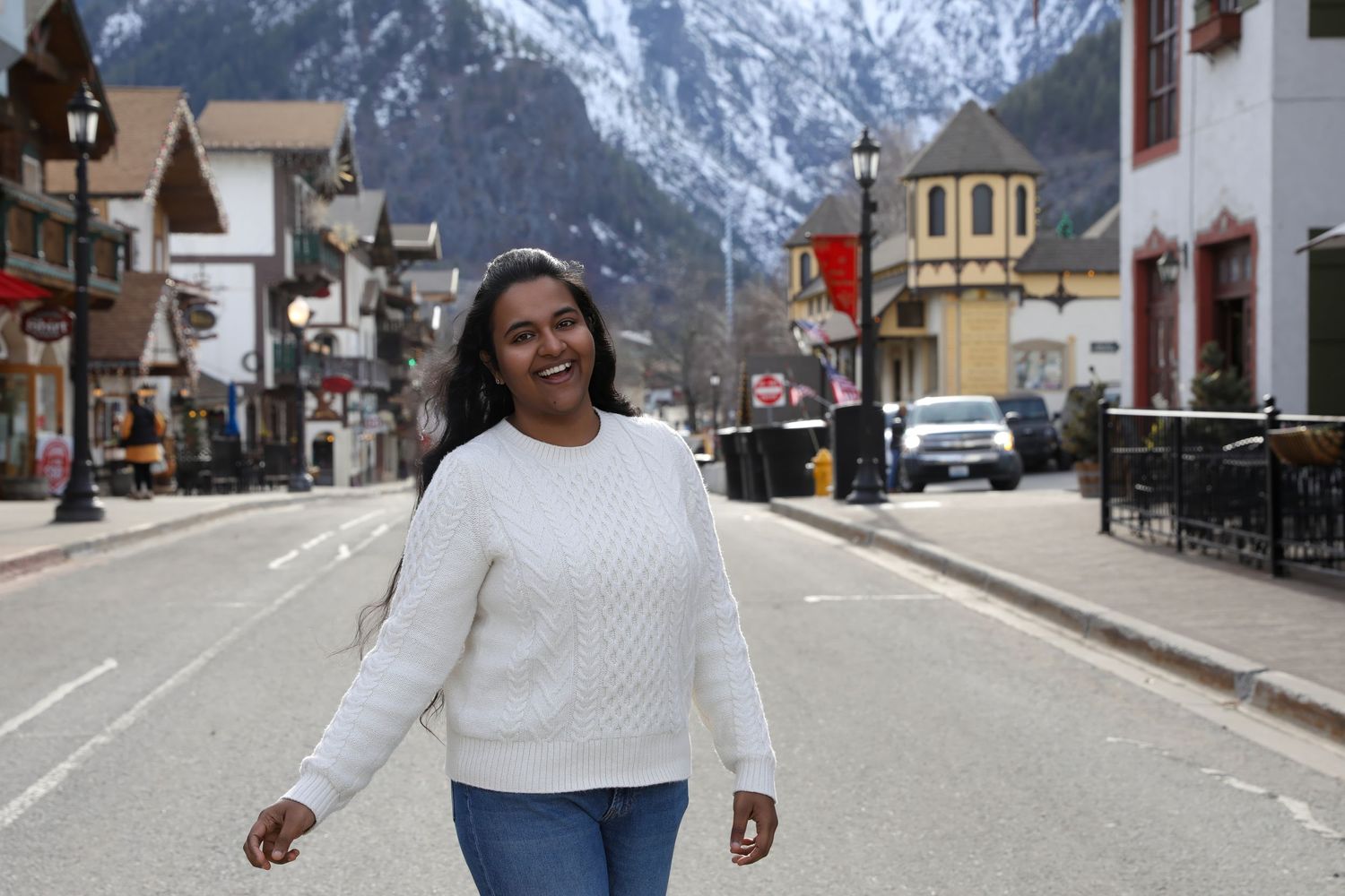 Woman in white sweater walking on a mountain town street with snow-capped peaks in the background.