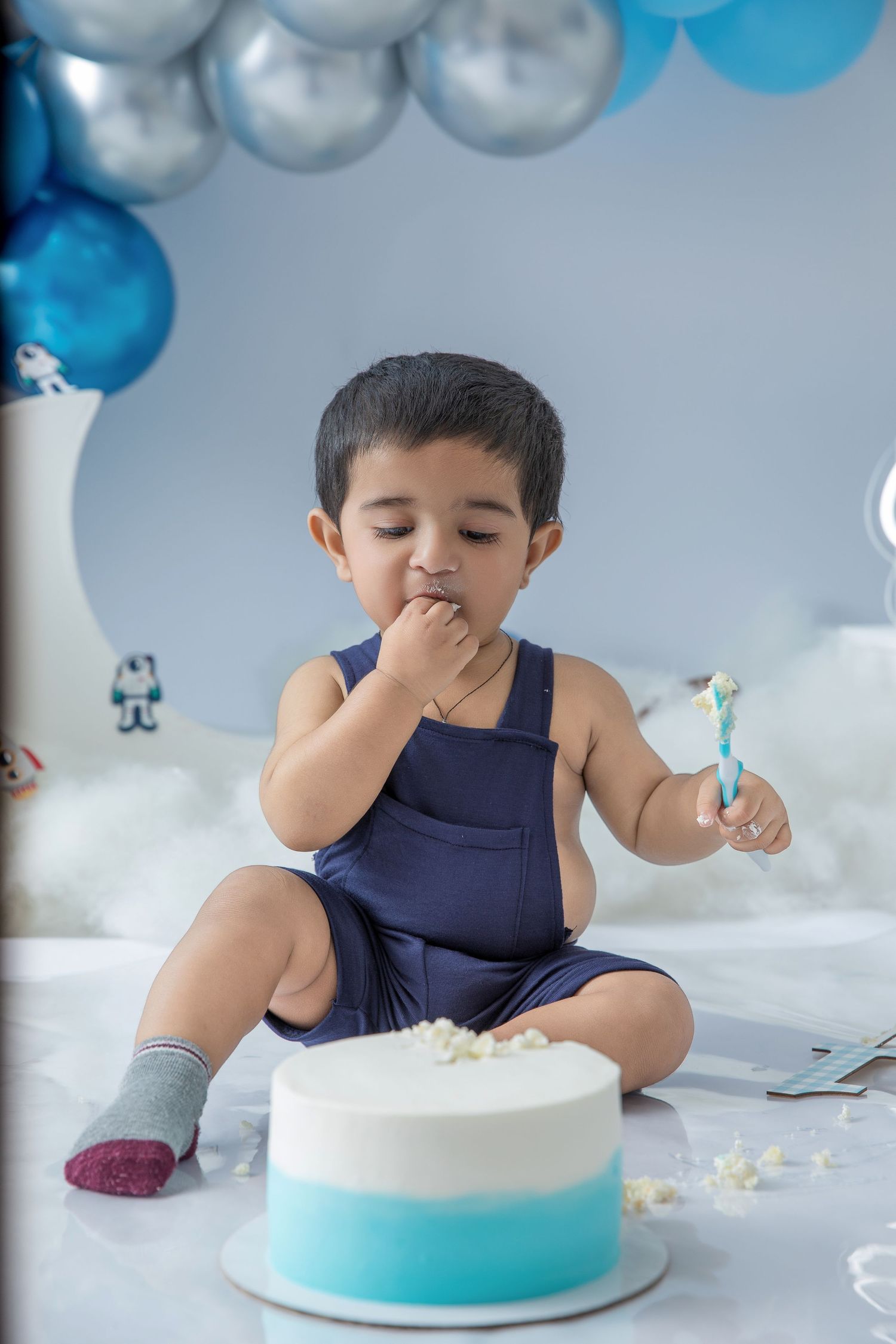 Cake smash photography session with blue and silver decor showing a taste test moment.