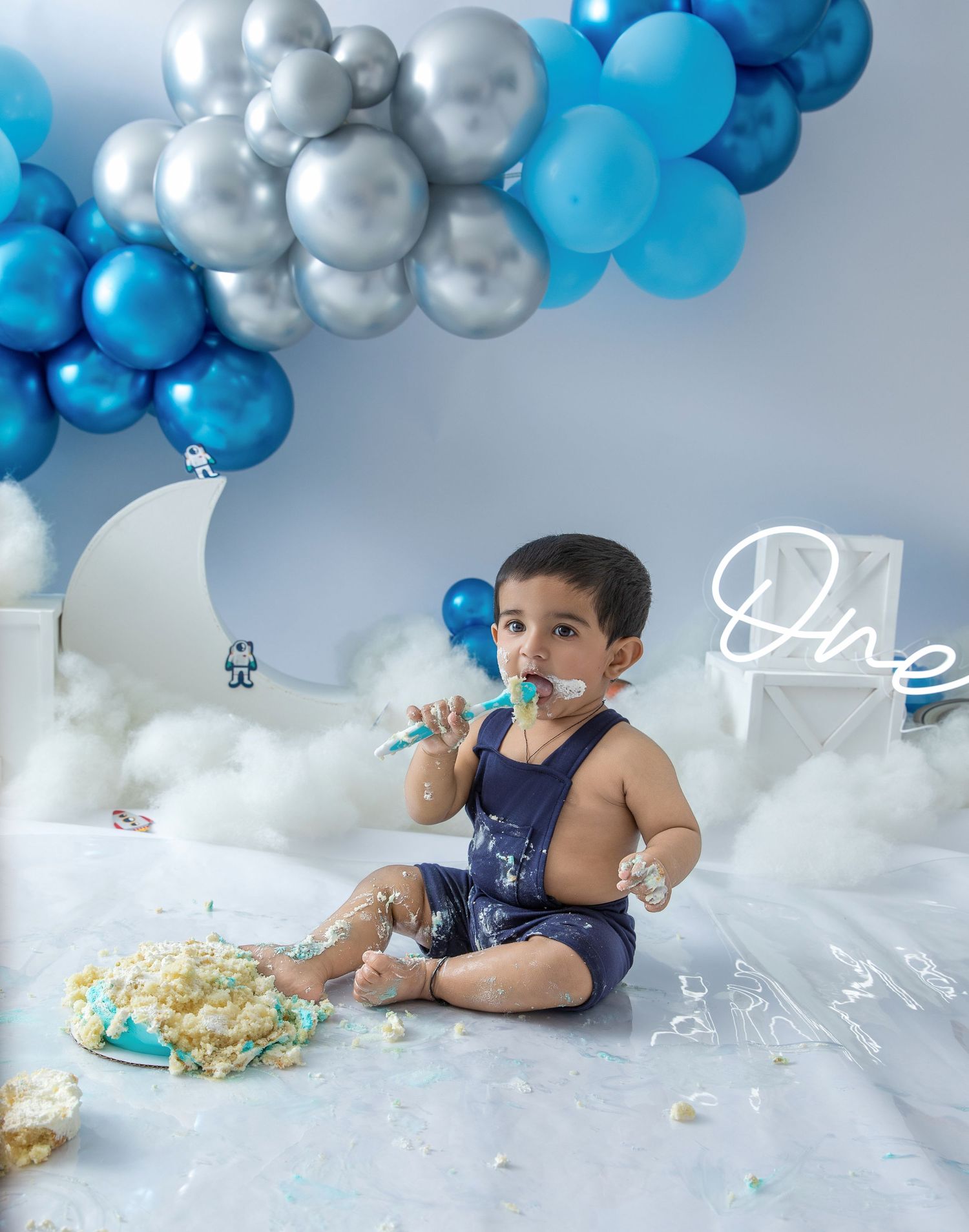 A cake smash photo session with blue and silver balloon decorations against a white backdrop.
