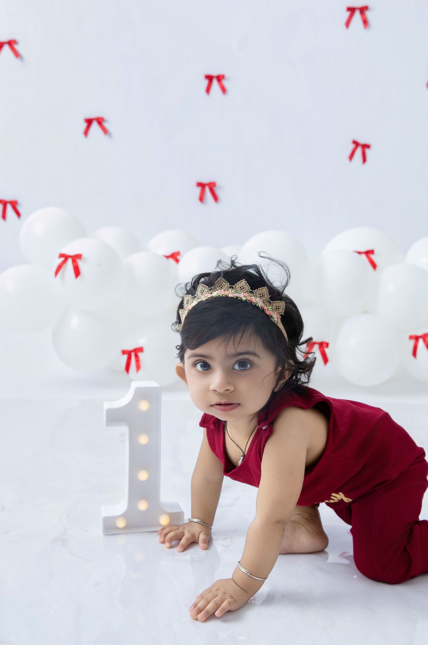 Baby crawling on white floor with number one light decoration and balloons.