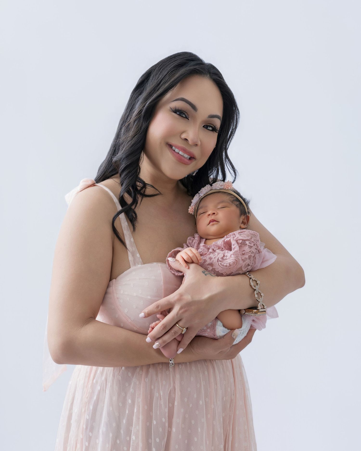 Smiling mother in a pink dress holding her sleeping newborn baby dressed in a pink floral outfit.