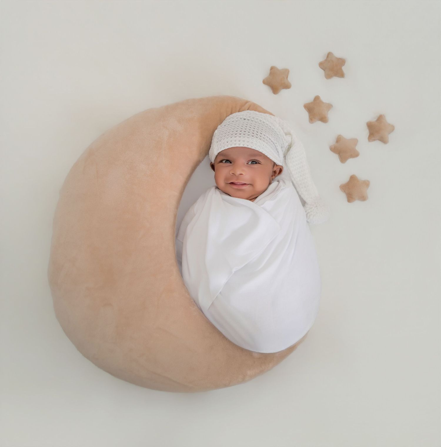 Newborn baby swaddled in white, smiling on a crescent moon pillow with wooden stars, perfect nursery photo.
