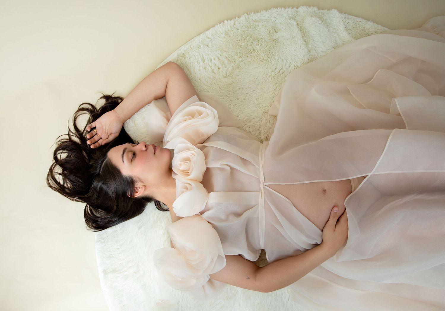 Woman in white dress lying gracefully on cream couch with soft plush decorations.