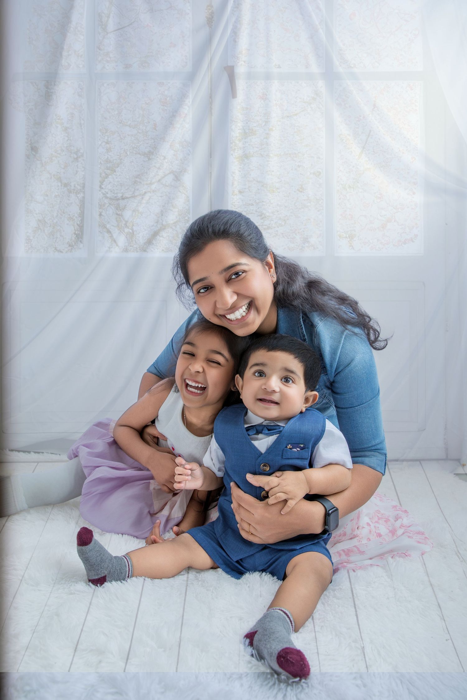 Family members share playful moments while sitting and hugging on a white floor against a light backdrop.
