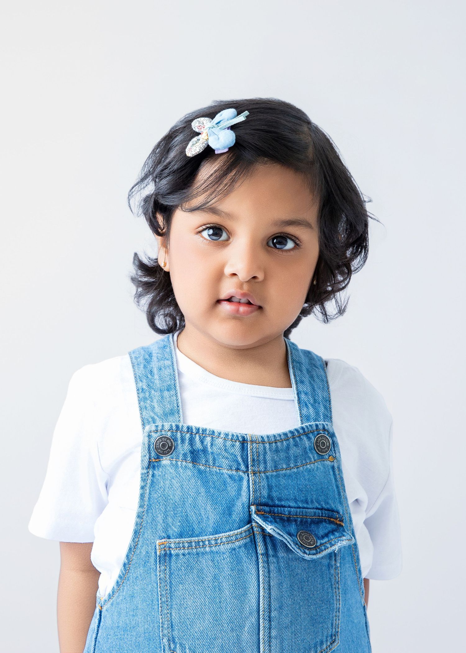 Young child in denim overalls and hair bows smiles while posing for portraits.