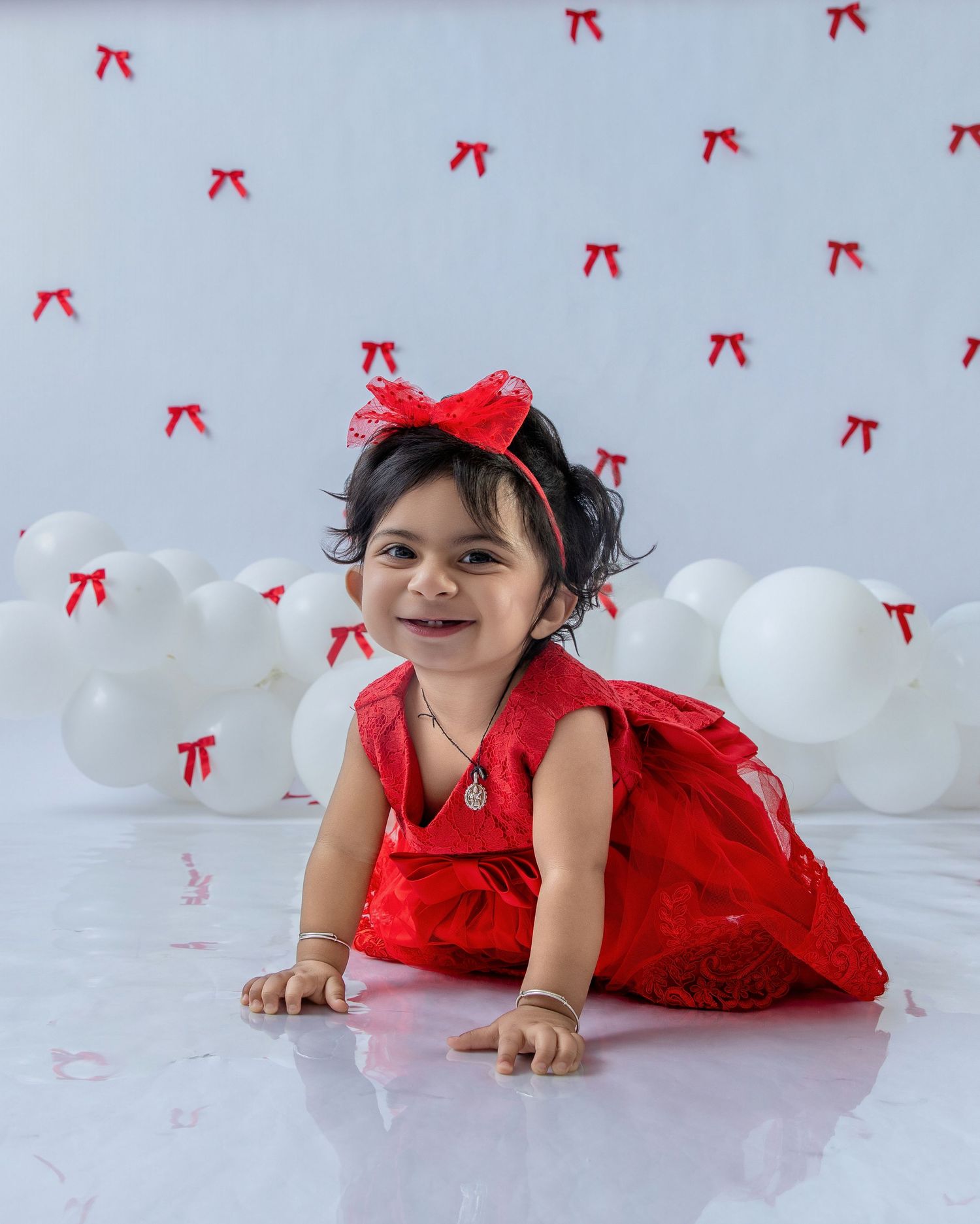 A child in a red lace dress lies on a white floor with red bows decorating the background.