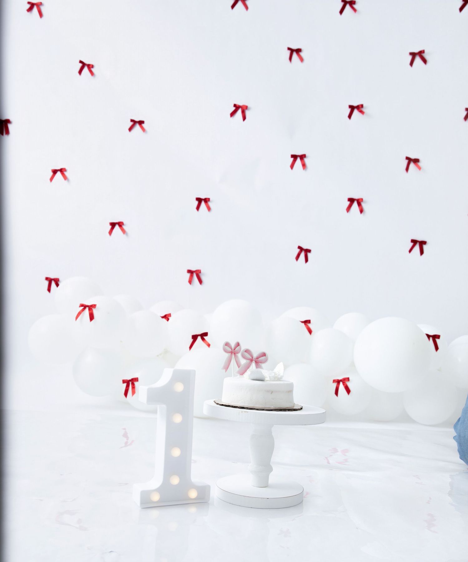 White studio setup with illuminated number one, balloons, and red bow decorations.