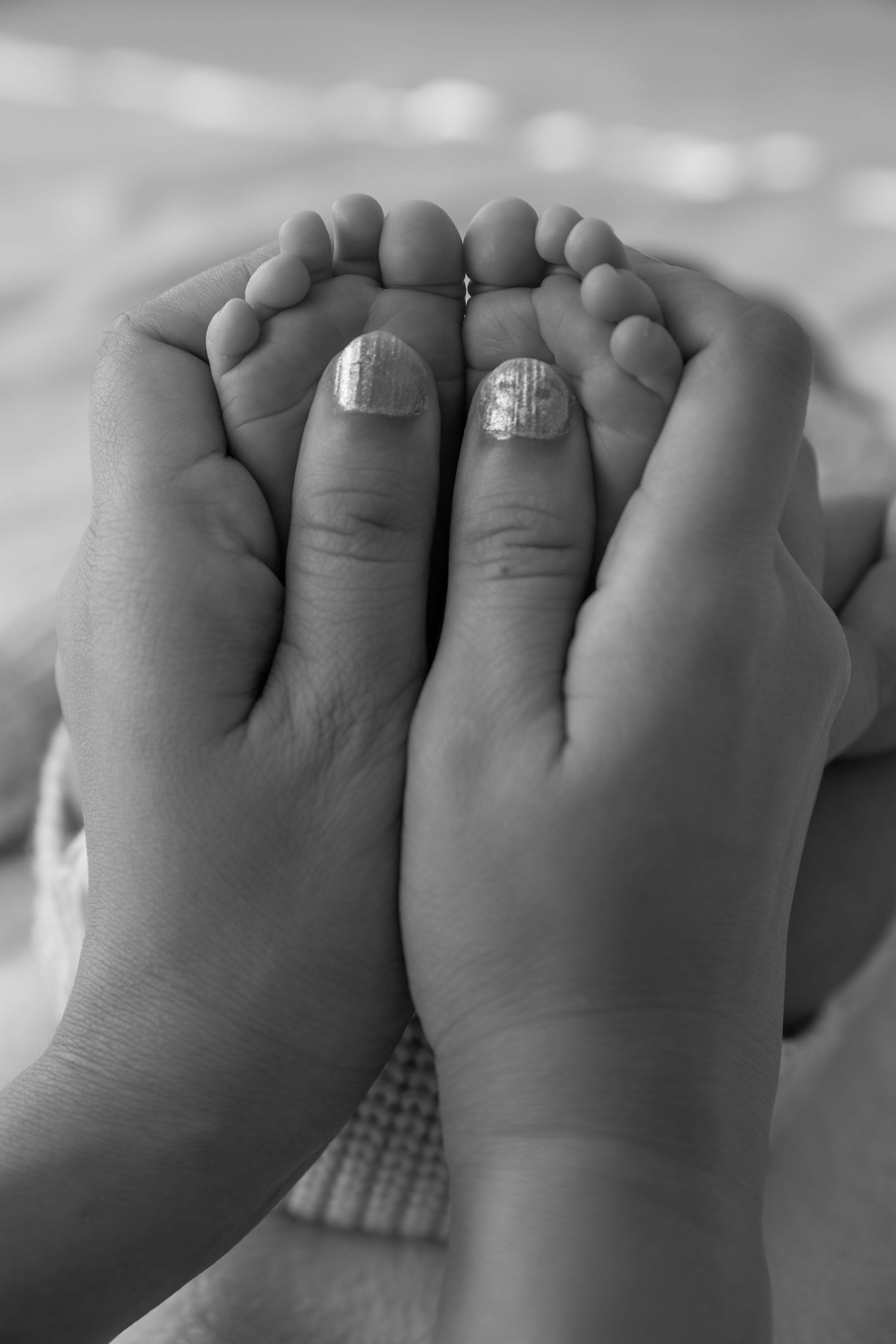 A close-up black and white photograph of adult hands gently cradling tiny baby feet with sparkly nail polish.