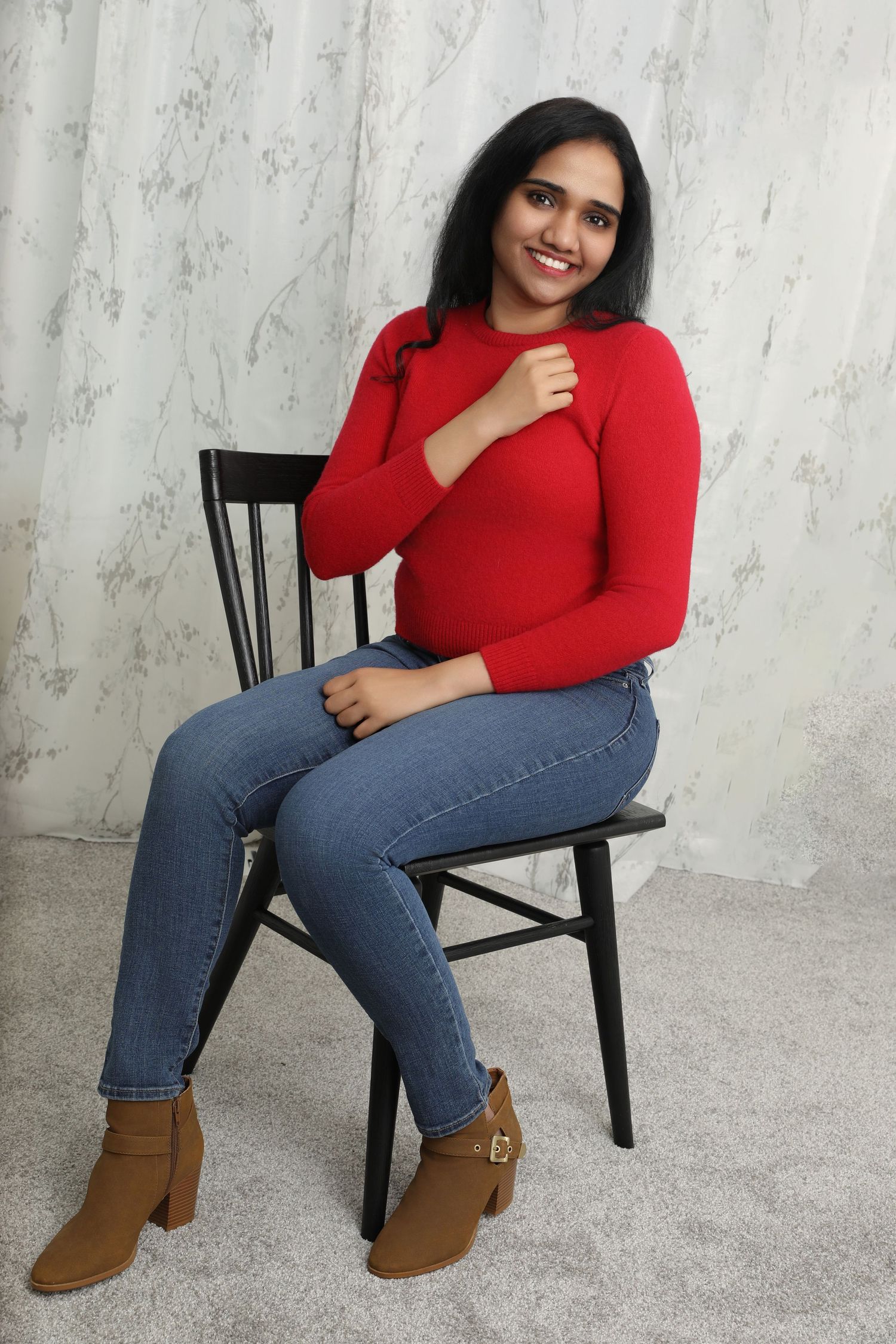 A cozy winter outfit featuring a red sweater, jeans and brown ankle boots on a black chair.