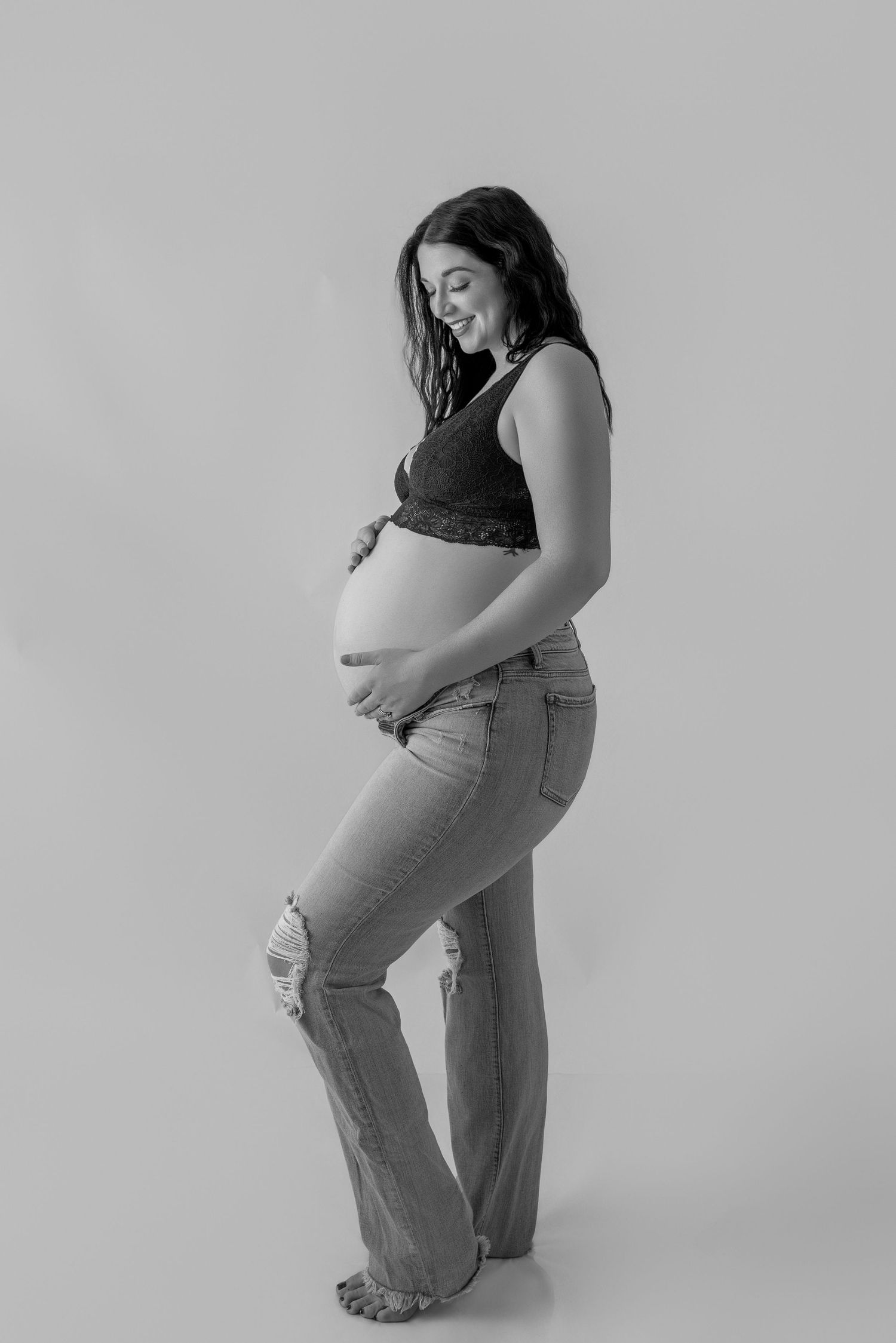 A series of black and white maternity photos showing a pregnant person in casual clothing posing against a simple backdrop.